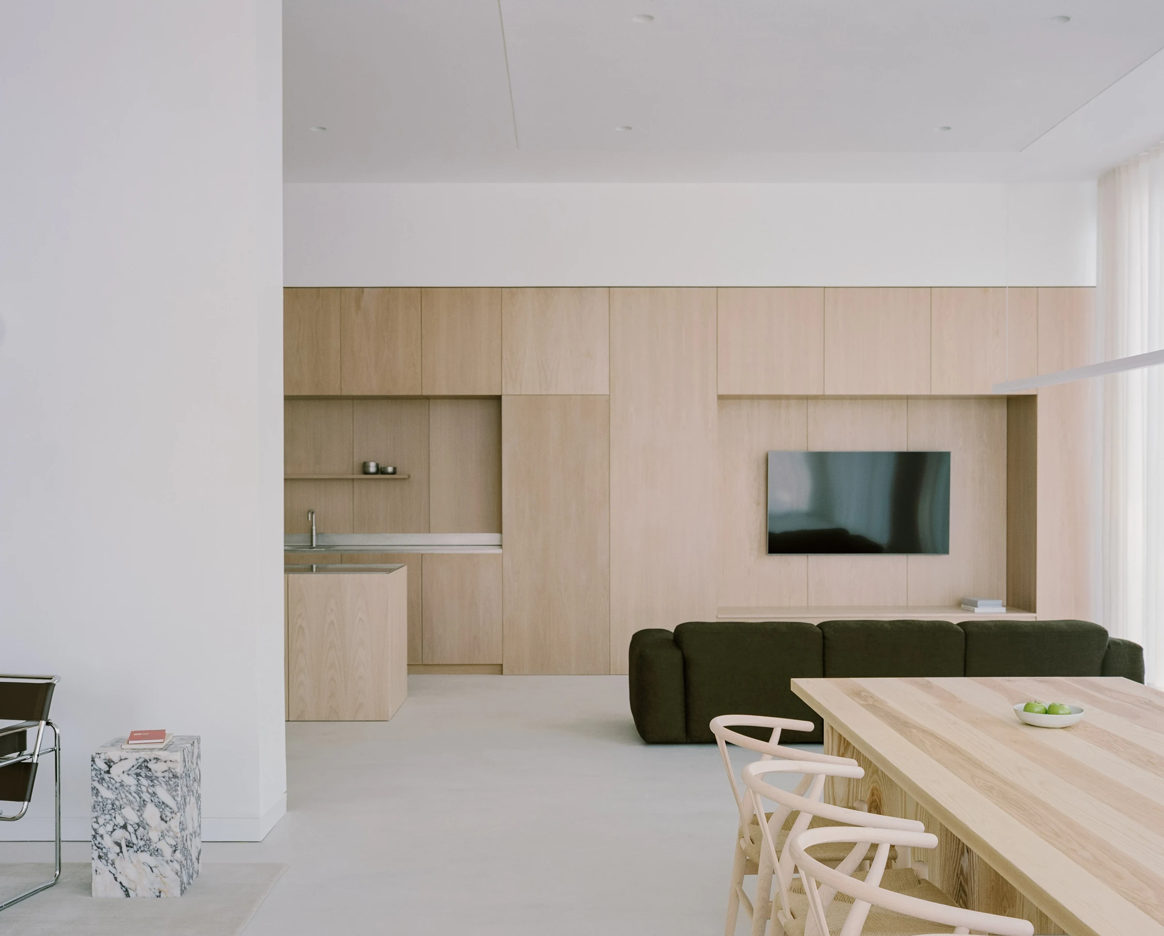 Cherry Orchard by Actual Office, photographed by Nick Dearden — Lower-floor study of the Knoll Wassily chair set against the floor-to-ceiling white voile, a small hardback book and water glass on the concrete floor at left, daylight pulling green and…