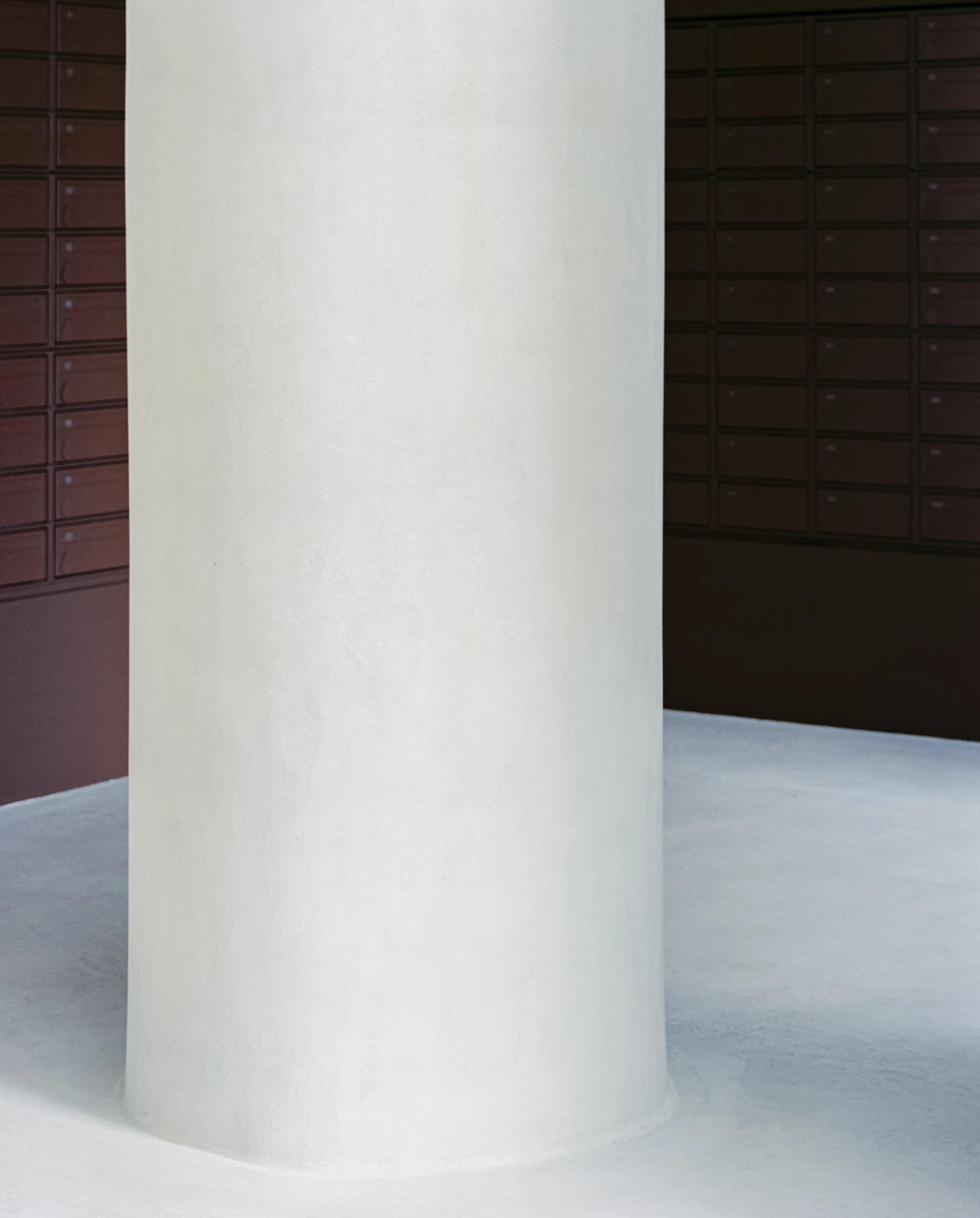 Cherry Orchard by Actual Office, photographed by Nick Dearden — Tight study of the plastered column standing in front of the deep cocoa mailbox wall: the column's matte lime-plaster finish catching cool light, the brown wall behind organised into a grid…