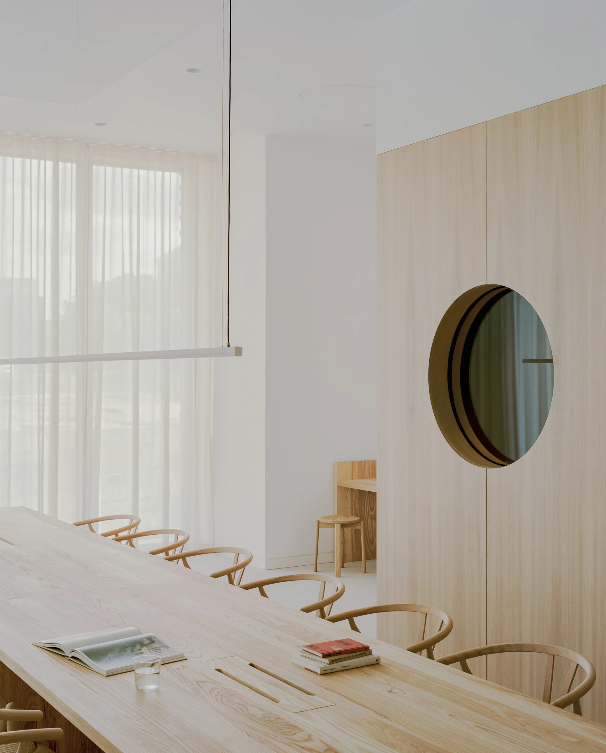 Cherry Orchard by Actual Office, photographed by Nick Dearden — Reading corner: a Menu Knitting lounge chair in cognac leather with a pale travertine side table, set against floor-to-ceiling cream voile curtaining that traces the curve of the room, an…