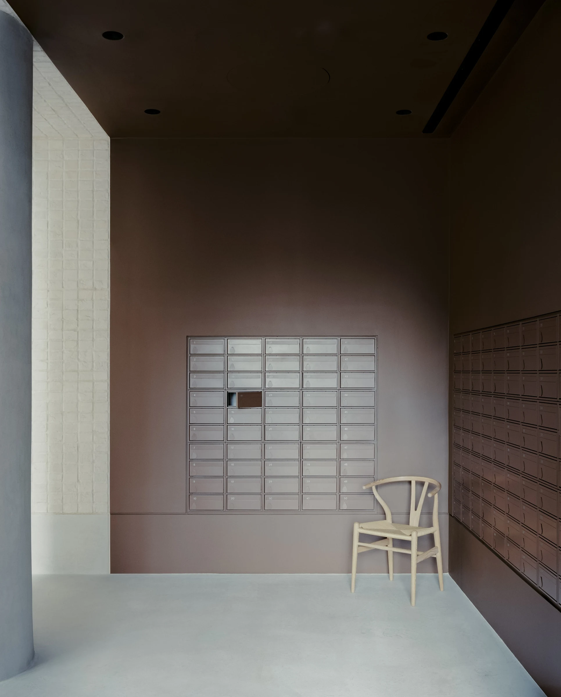 Cherry Orchard by Actual Office, photographed by Nick Dearden — Top-down detail of the concierge desk: stainless surface broken by a single circular drop-point, the brushed metal catching the pale wash of the white-painted brick wall behind.