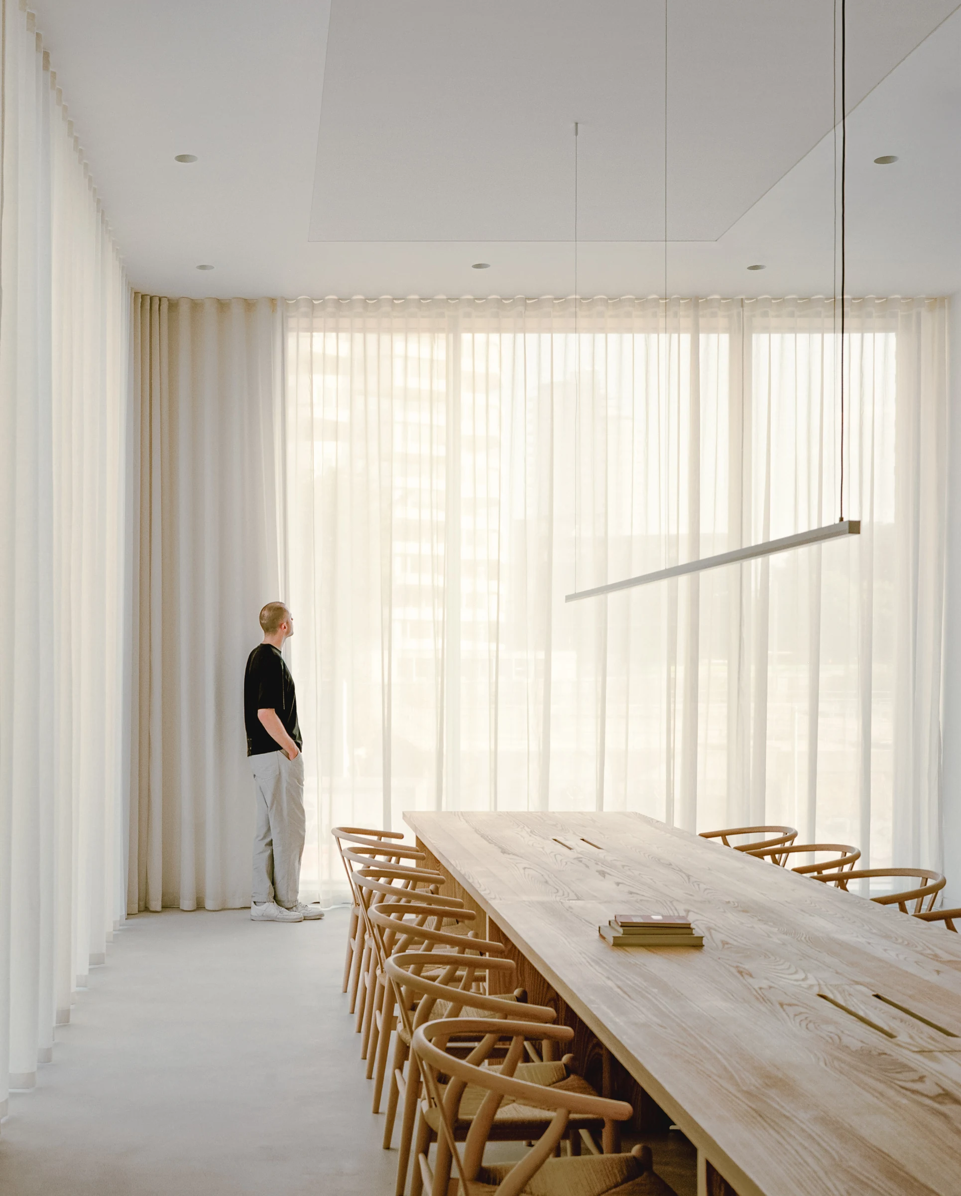 Cherry Orchard by Actual Office, photographed by Nick Dearden — A double-height communal lounge: oak joinery wall to the right, the soffit dropped above to register a clearer ceiling line, a circular dark mirror set into the wood like a porthole, ash…