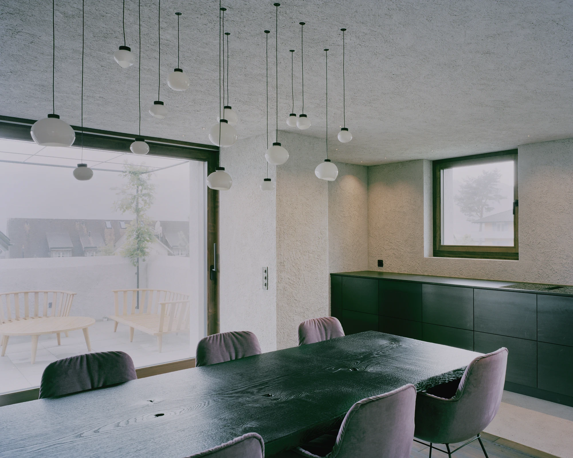 Tower house Vaduz by Schreiber Architekten, photographed by Barbara Buehler — a roughsawn dining table and pendant lights stand before a sliding glass wall onto the terrace.