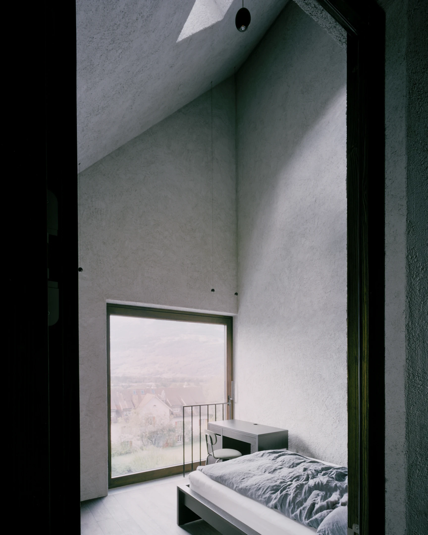 Tower house Vaduz by Schreiber Architekten, photographed by Barbara Buehler — under the bare pitch of the roof, a top-floor bedroom faces a tall window over the foggy valley.