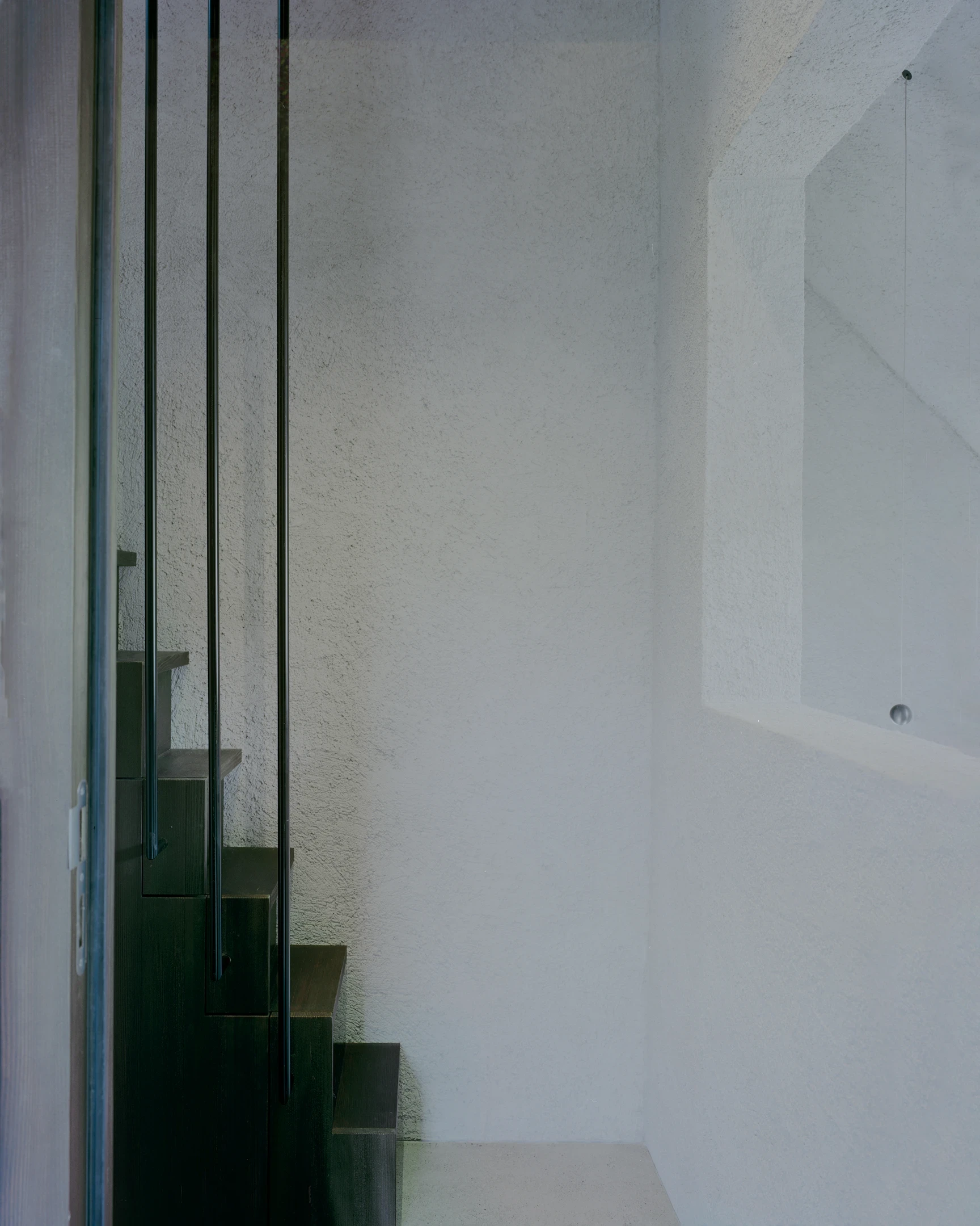 Tower house Vaduz by Schreiber Architekten, photographed by Barbara Buehler — a dark timber stair with a slim steel rail rises against a white plastered shaft lit from above.