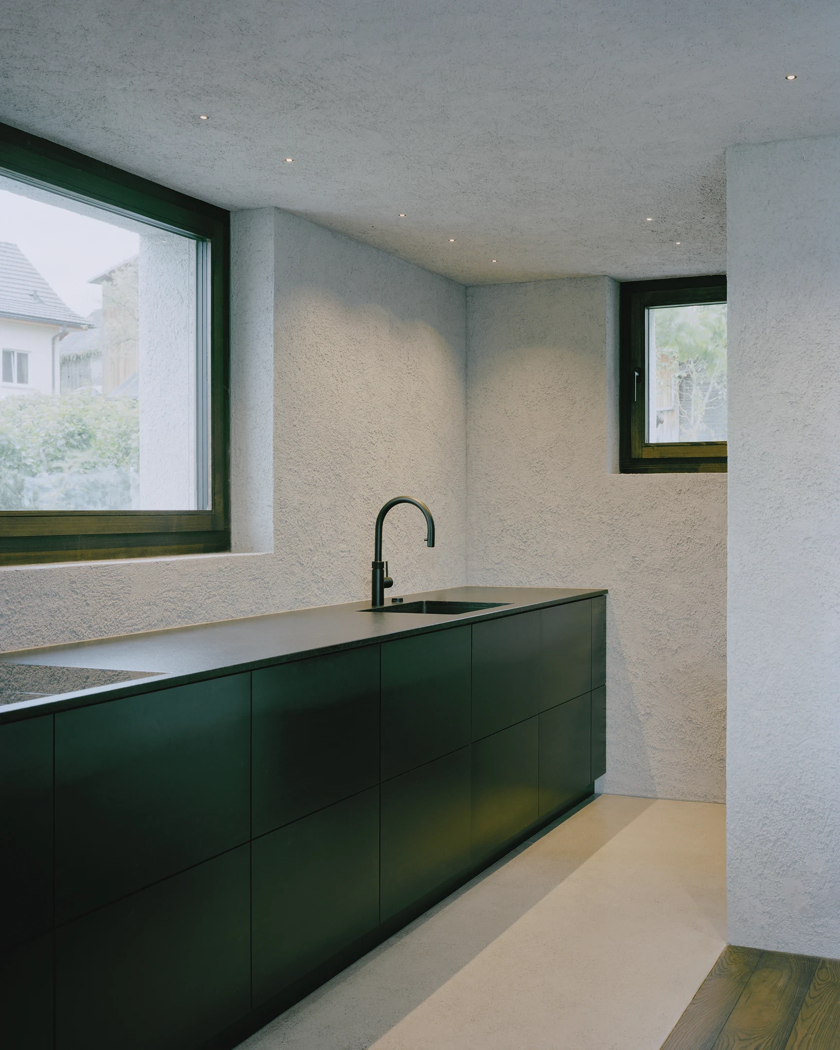 Tower house Vaduz by Schreiber Architekten, photographed by Barbara Buehler — a dark green kitchen run sits below coarse gray lime-plaster walls and a spruce-framed window.
