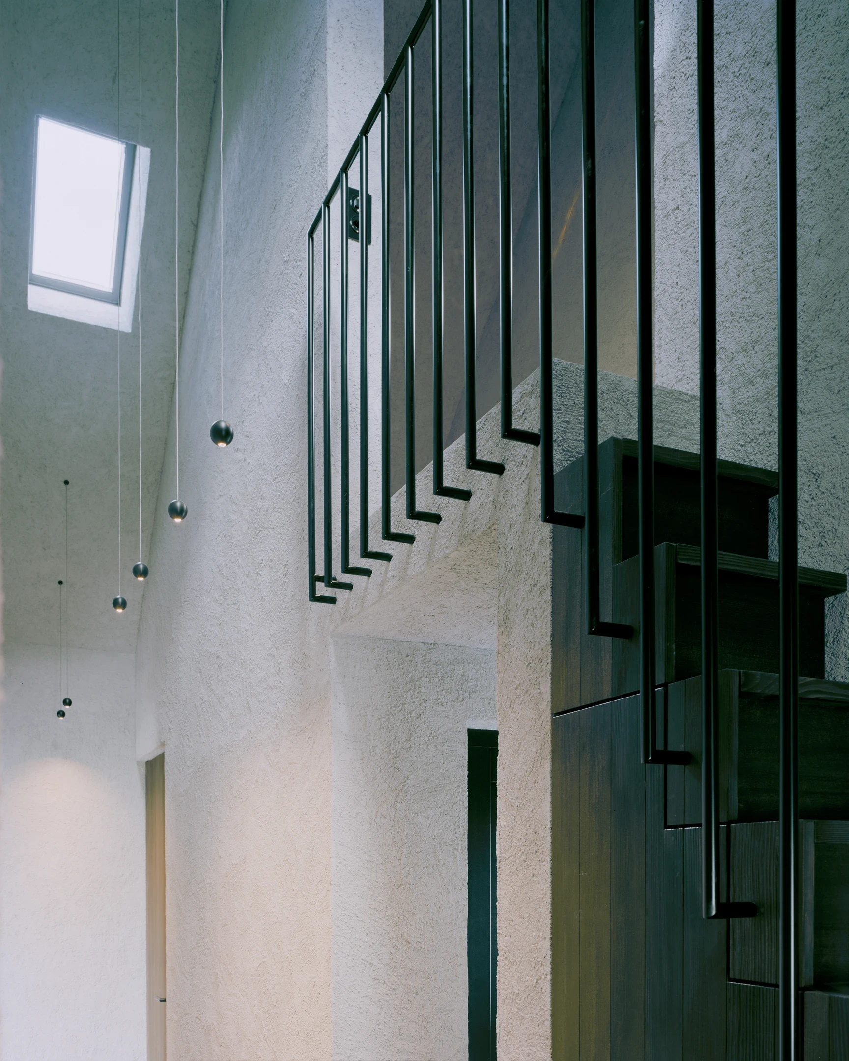 Tower house Vaduz by Schreiber Architekten, photographed by Barbara Buehler — the stair climbs past a clerestory window, slim black balustrades cutting across the coarse gray plaster.