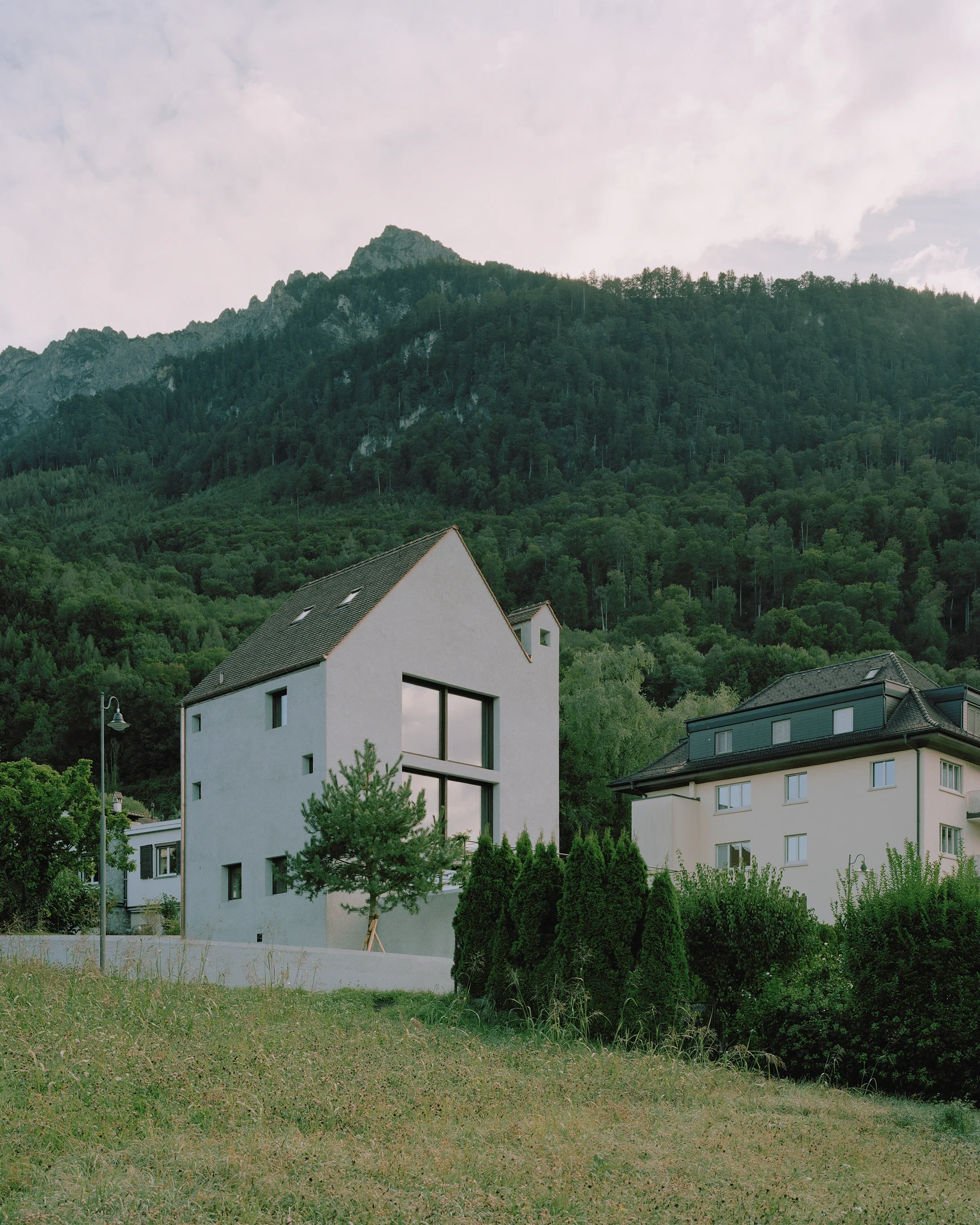 Tower house Vaduz by Schreiber Architekten, photographed by Barbara Buehler — seen from the meadow, the tall gable and a large corner window face the forested Three Sisters massif.