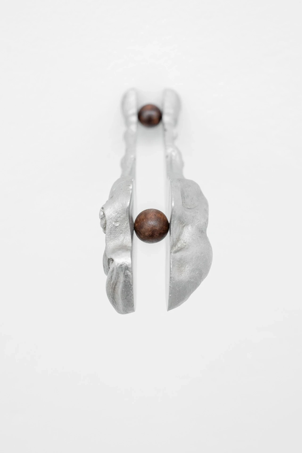 Double Star by Paola Siri Renard, photographed by Dirk Tacke — a frontal view of the mirrored split fragment, two dark wooden balls held in the narrow interstice between its twin polished faces.