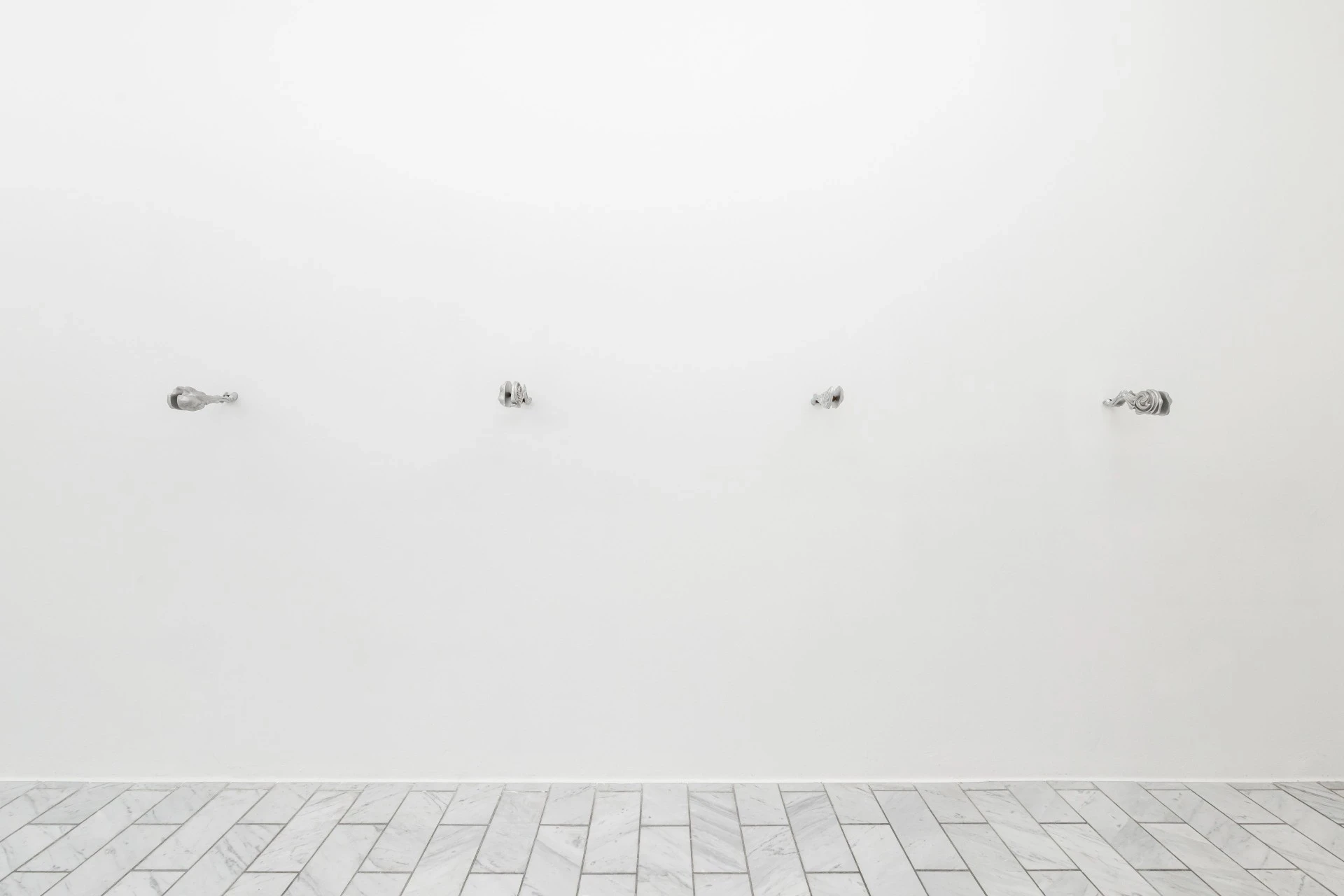 Double Star by Paola Siri Renard, photographed by Dirk Tacke — four small polished aluminum pieces punctuate a long white wall above the marble herringbone floor.