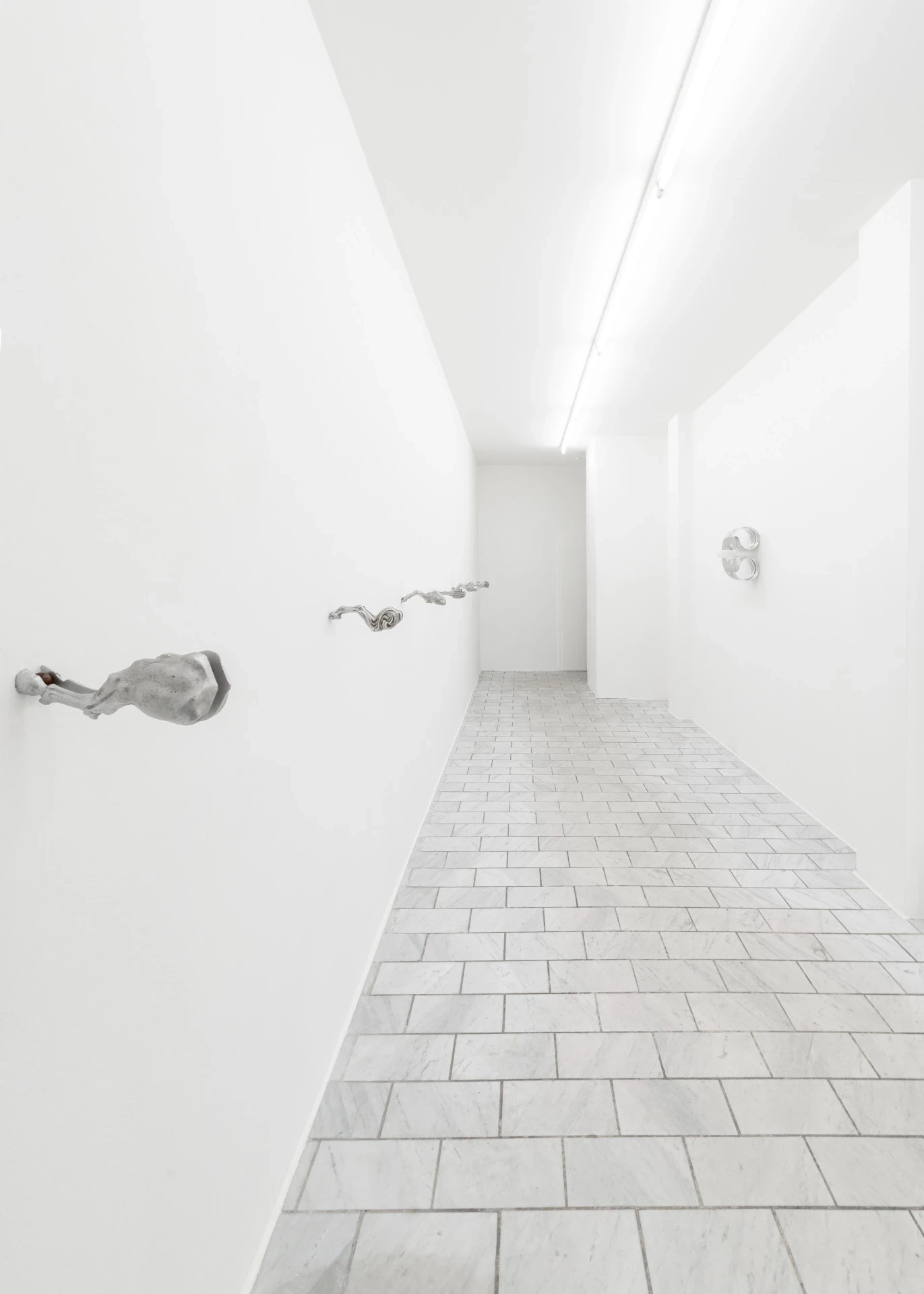 Double Star by Paola Siri Renard, photographed by Dirk Tacke — three wall-mounted works stagger down a marble corridor toward a mirror-polished piece at its far end.