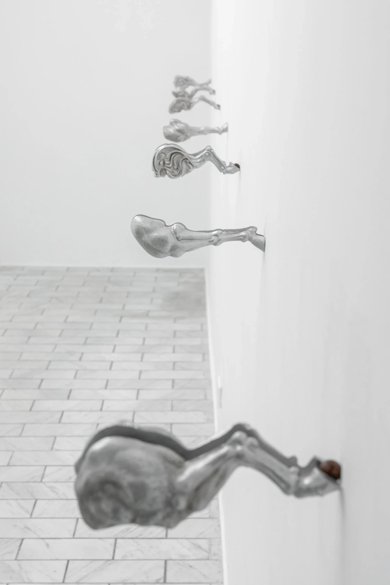 Double Star by Paola Siri Renard, photographed by Dirk Tacke — wall-mounted fragments recede down a corridor, a skeletal leg and swollen haunch jutting from the white wall above the marble herringbone floor.