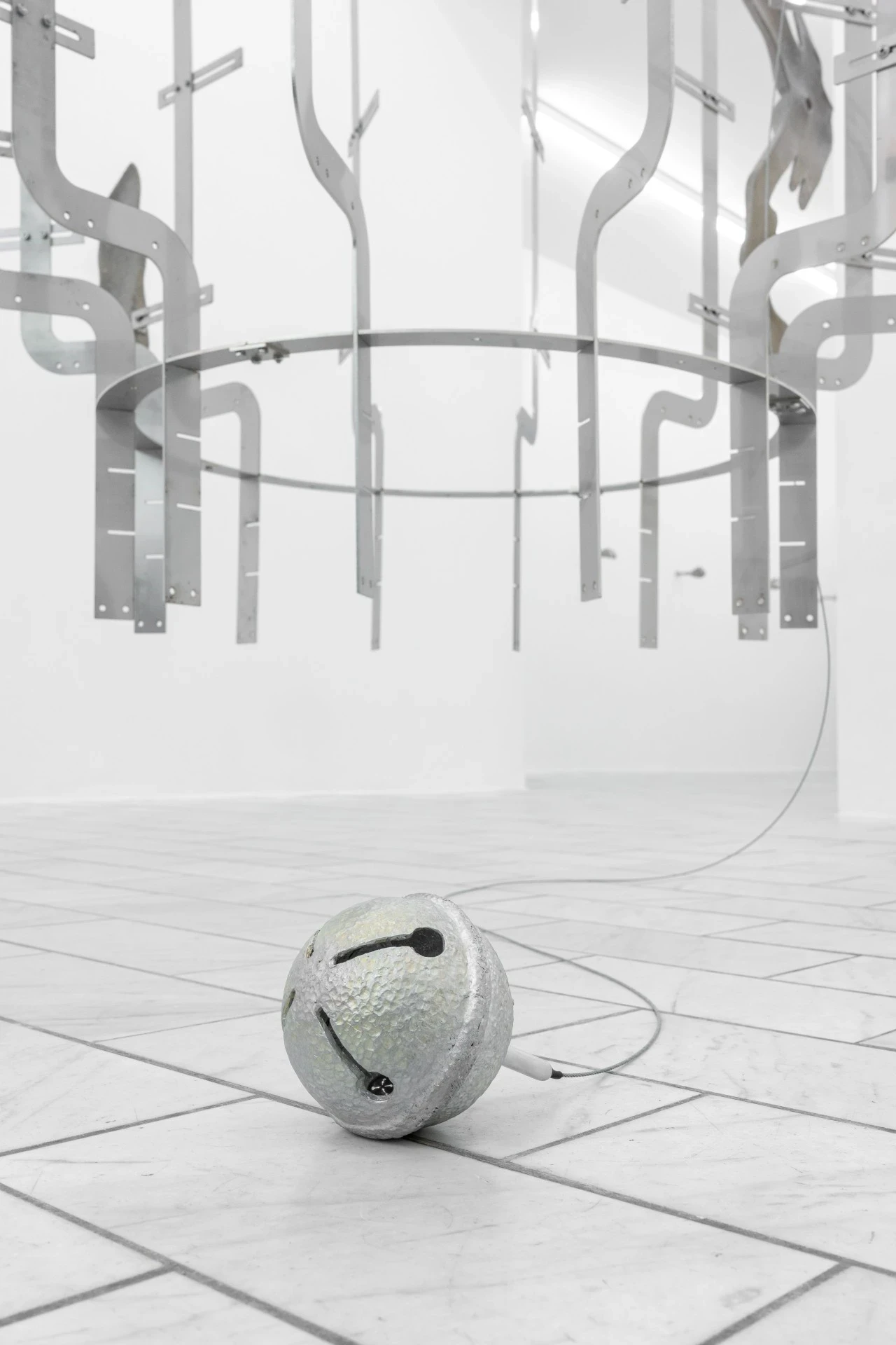 Double Star by Paola Siri Renard, photographed by Dirk Tacke — the empty stainless-steel ring of the armature seen from below, slotted uprights curling outward and a hammered jingle bell wired on the tiles.