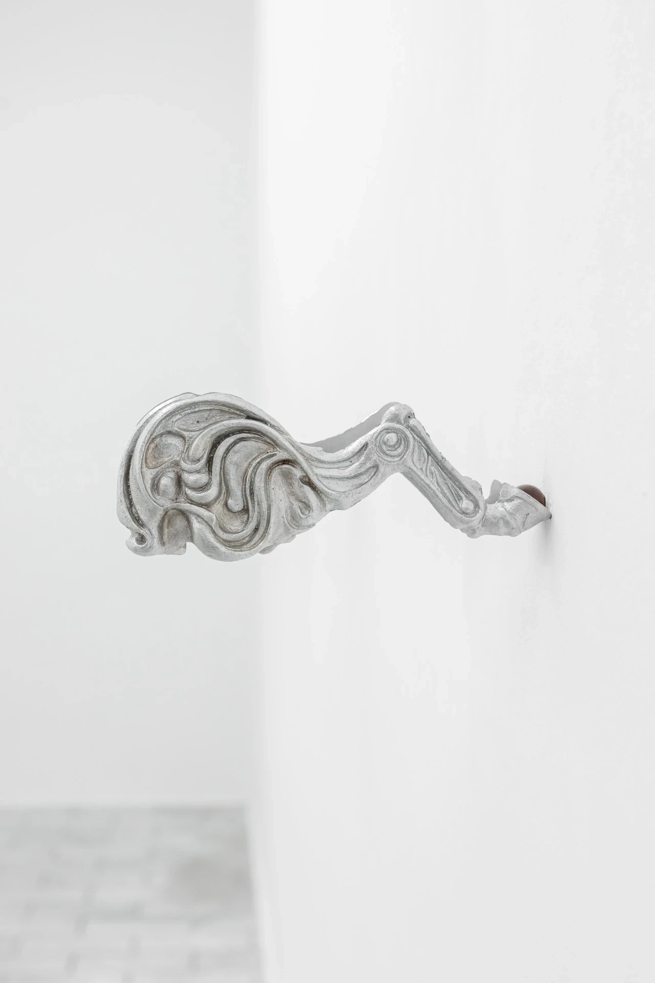 Double Star by Paola Siri Renard, photographed by Dirk Tacke — a single fragment of whiplash scrollwork projects from a corner of the white wall, ornament thinning into a bony tip at its end.