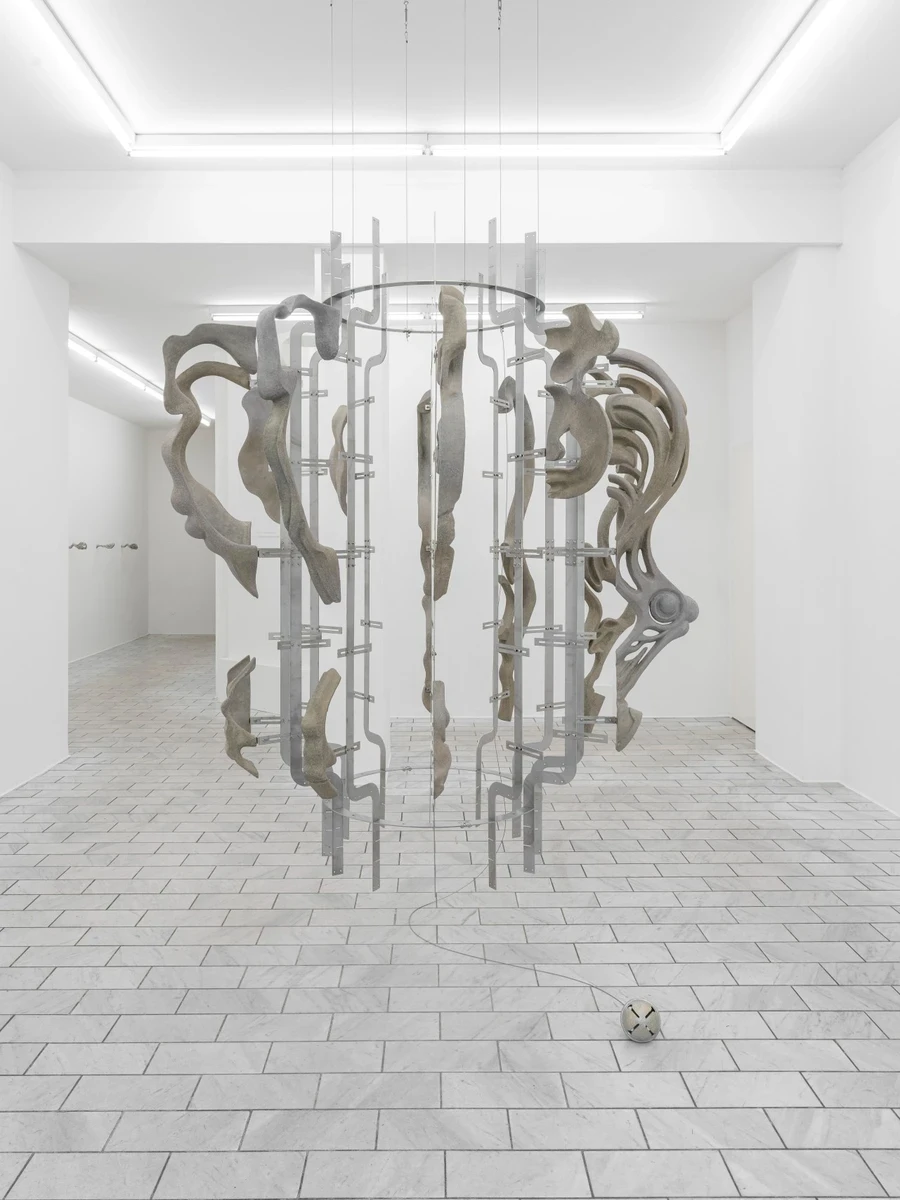 Double Star by Paola Siri Renard, photographed by Dirk Tacke — the suspended twelve-part figure reads almost as a single rearing animal, ringed by stainless-steel armatures with a hammered jingle bell resting on the marble floor below.