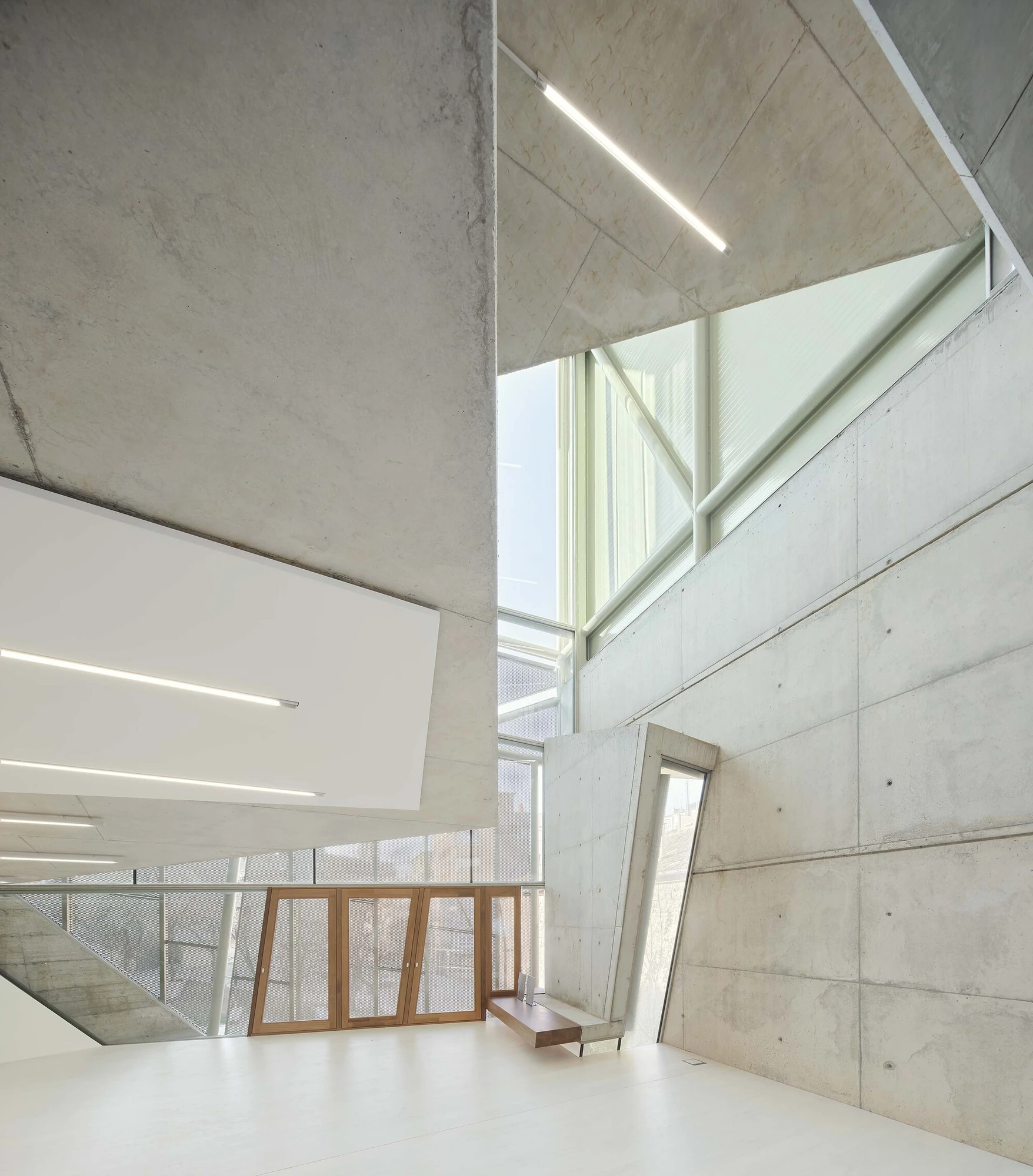 Entrance Façade of the Baroque Museum of Catalonia by David Closes, photographed by Adrià Goula, José Hevia — Faceted board-formed concrete planes meet a wedge of glazing and translucent polycarbonate, oak window frames leaning against the wall on a…