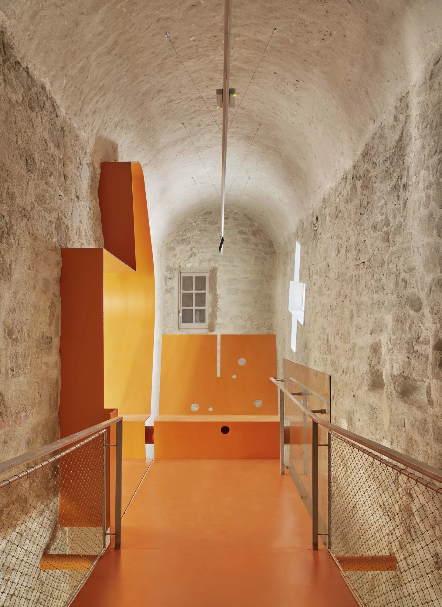 Entrance Façade of the Baroque Museum of Catalonia by David Closes, photographed by Adrià Goula, José Hevia — A rough limestone barrel-vaulted passage lined with an orange floor and folded orange panels, a small original window at the far end.