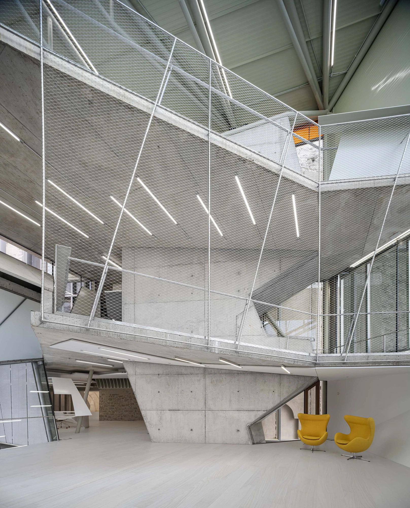Entrance Façade of the Baroque Museum of Catalonia by David Closes, photographed by Adrià Goula, José Hevia — A double-height interior of board-formed concrete and stainless mesh balustrades under a green roof structure, slot lighting overhead and two…