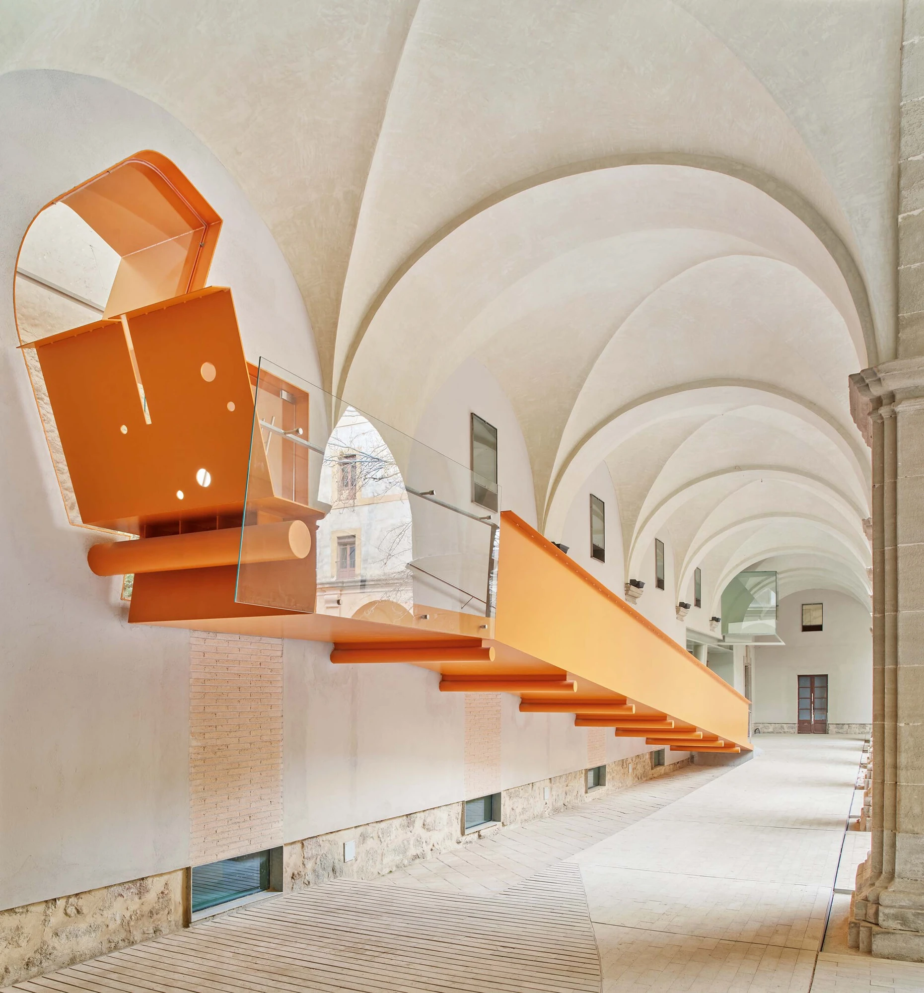 Entrance Façade of the Baroque Museum of Catalonia by David Closes, photographed by Adrià Goula, José Hevia — A white groin-vaulted cloister gallery where an orange steel beam and bench cantilever in a long line off the brick wall toward sunlight.