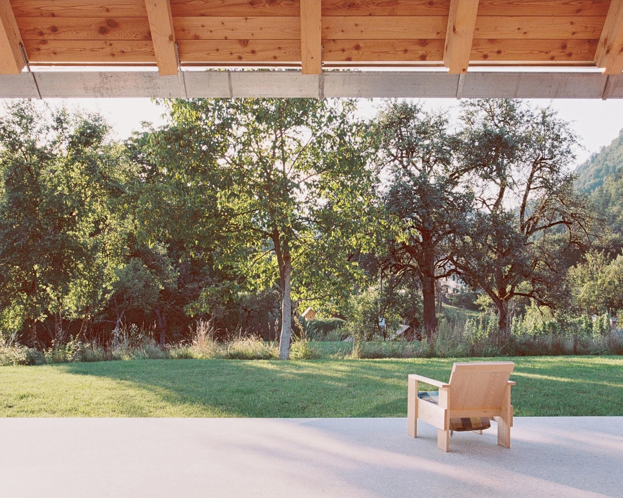 House Alva by Arhitekti Počivašek Petranovič, photographed by Urban Petranovič — The covered terrace under exposed timber joists, a larch lounge chair facing the orchard and distant hills.