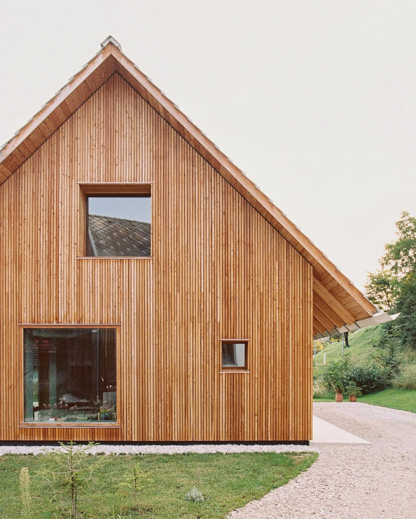 House Alva by Arhitekti Počivašek Petranovič, photographed by Urban Petranovič — The gable end clad in vertical larch boarding, punctured by two square windows above a gravel path.