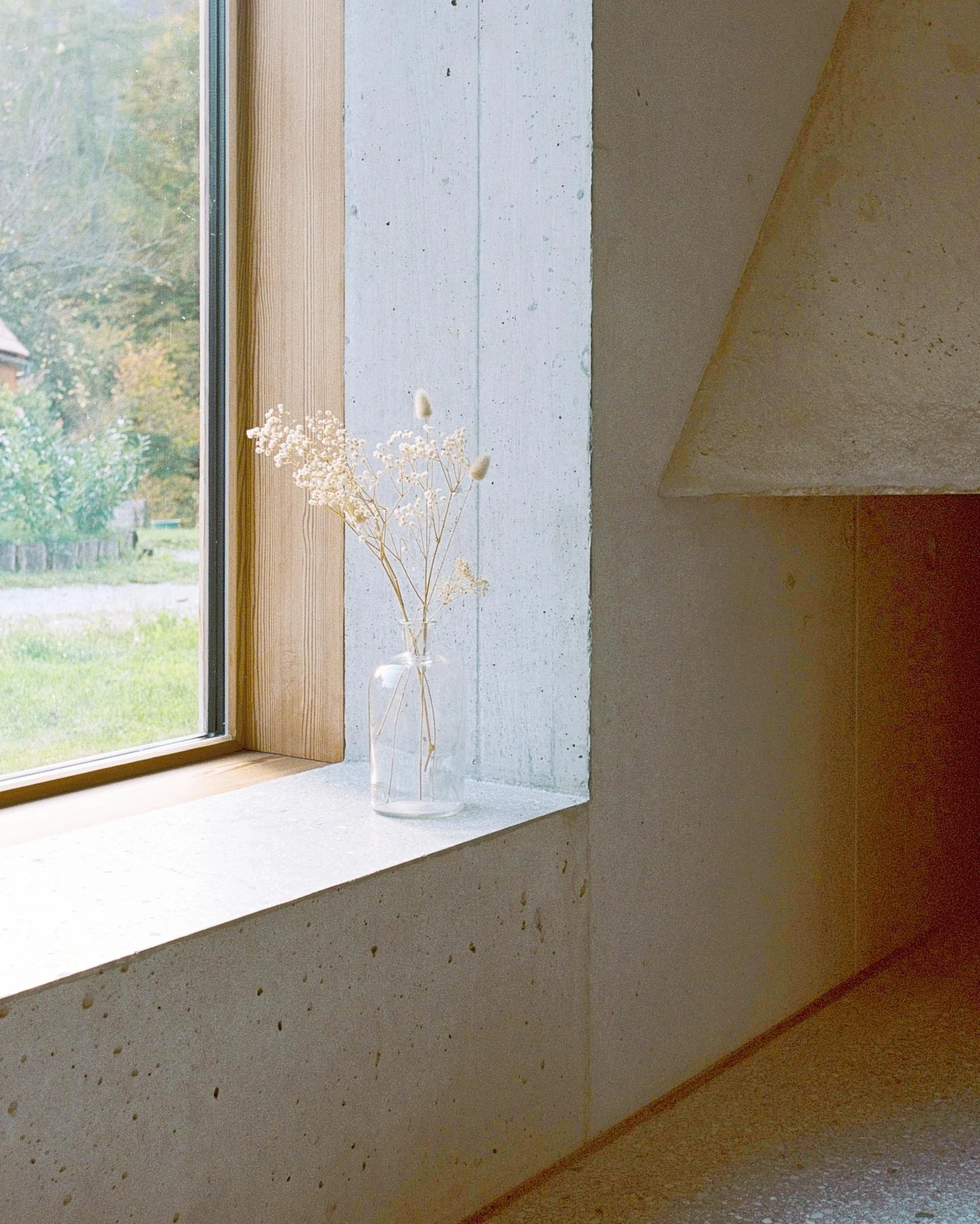 House Alva by Arhitekti Počivašek Petranovič, photographed by Urban Petranovič — A deep concrete window reveal holds dried flowers in a glass jar beside the cast edge of the fireplace.