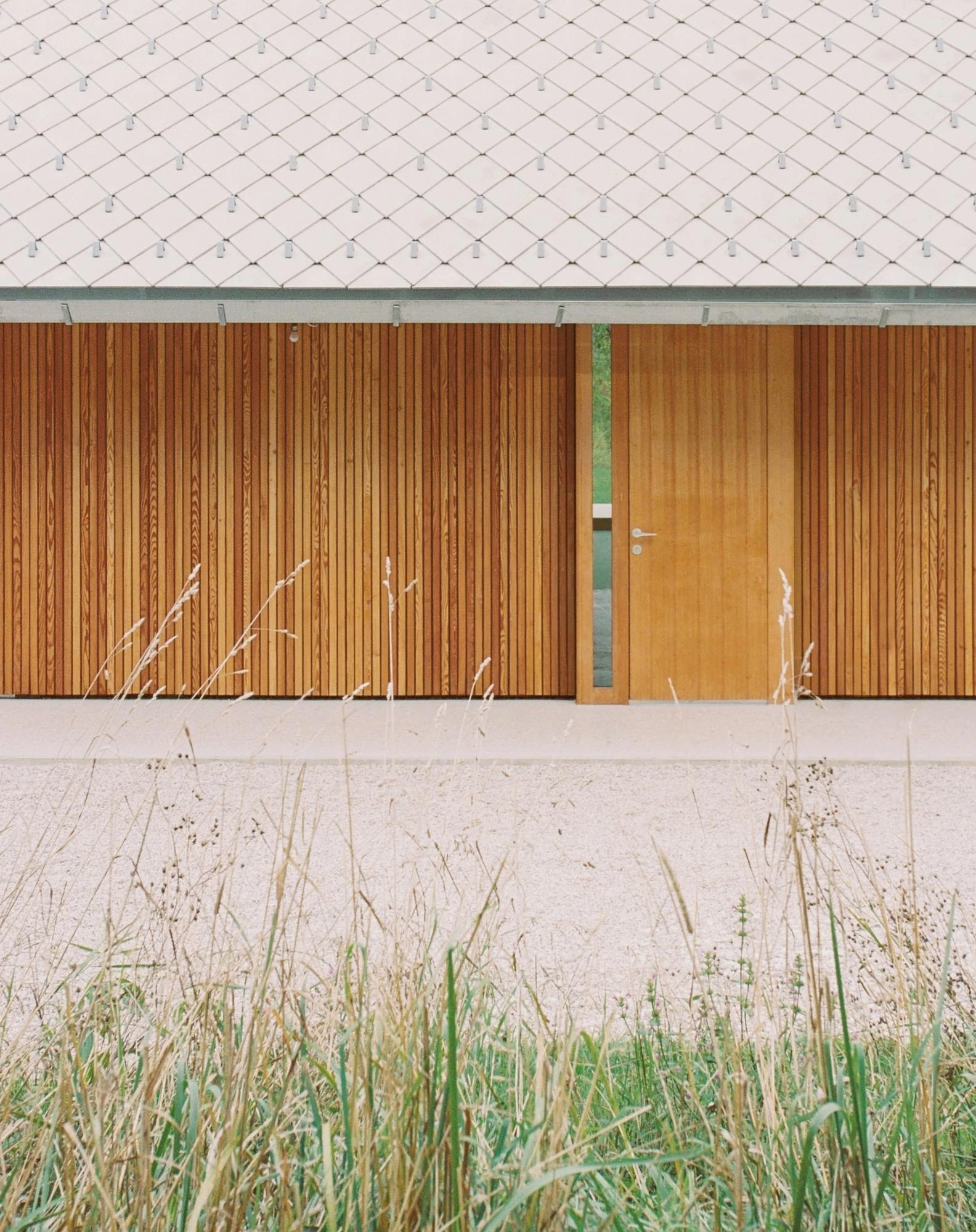 House Alva by Arhitekti Počivašek Petranovič, photographed by Urban Petranovič — A close view where the diamond concrete roof tiles meet sliding larch screens framing a single larch door.