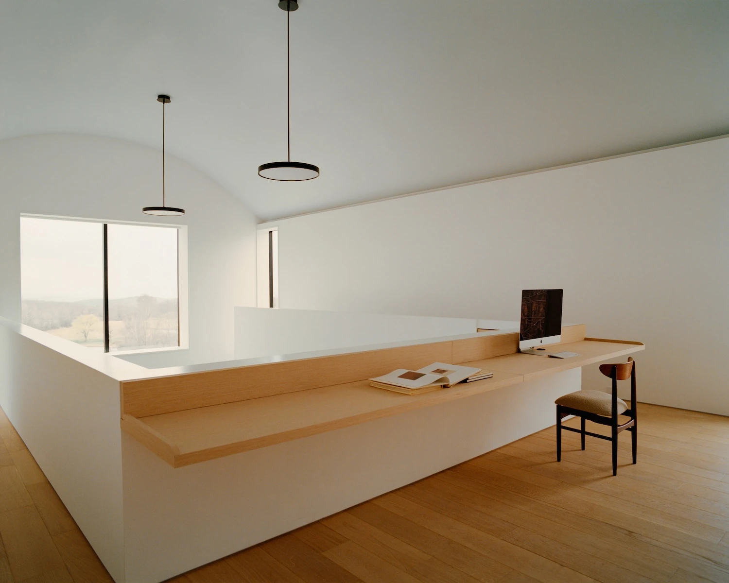 Schoolhouse by JG Neukomm Architecture, photographed by William Jess Laird — Two disc pendants hang under the barrel vault of the mezzanine office, lighting a built-in oak desk above a window onto the fields.