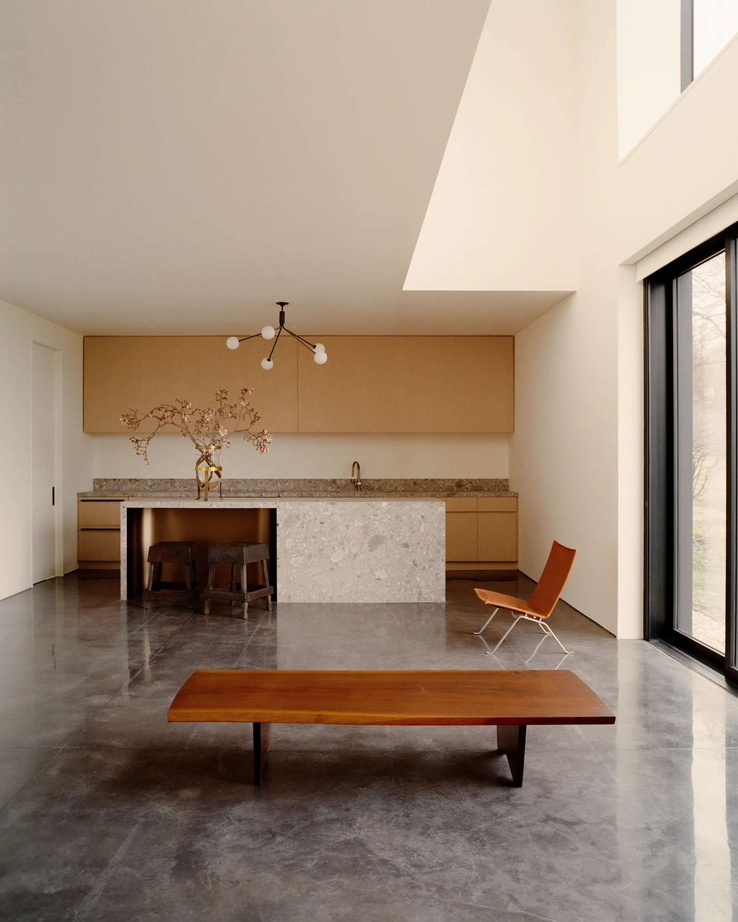 Schoolhouse by JG Neukomm Architecture, photographed by William Jess Laird — A terrazzo island and pale oak cabinetry anchor the kitchen, fronted by a low walnut bench on a sweep of polished concrete.