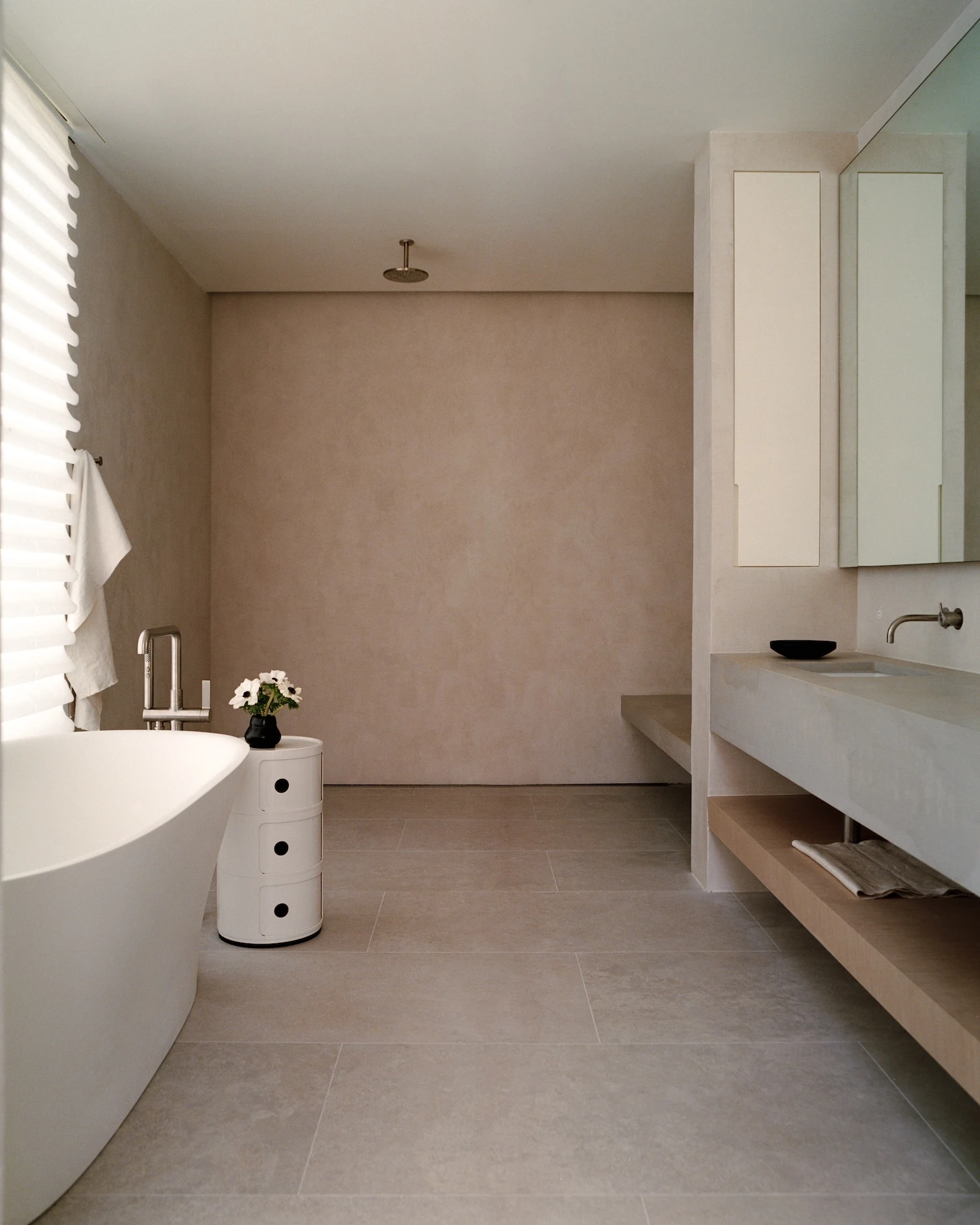 Schoolhouse by JG Neukomm Architecture, photographed by William Jess Laird — A freestanding tub and board-formed concrete vanity stand against limewashed plaster walls in a bathroom floored with large stone tile.