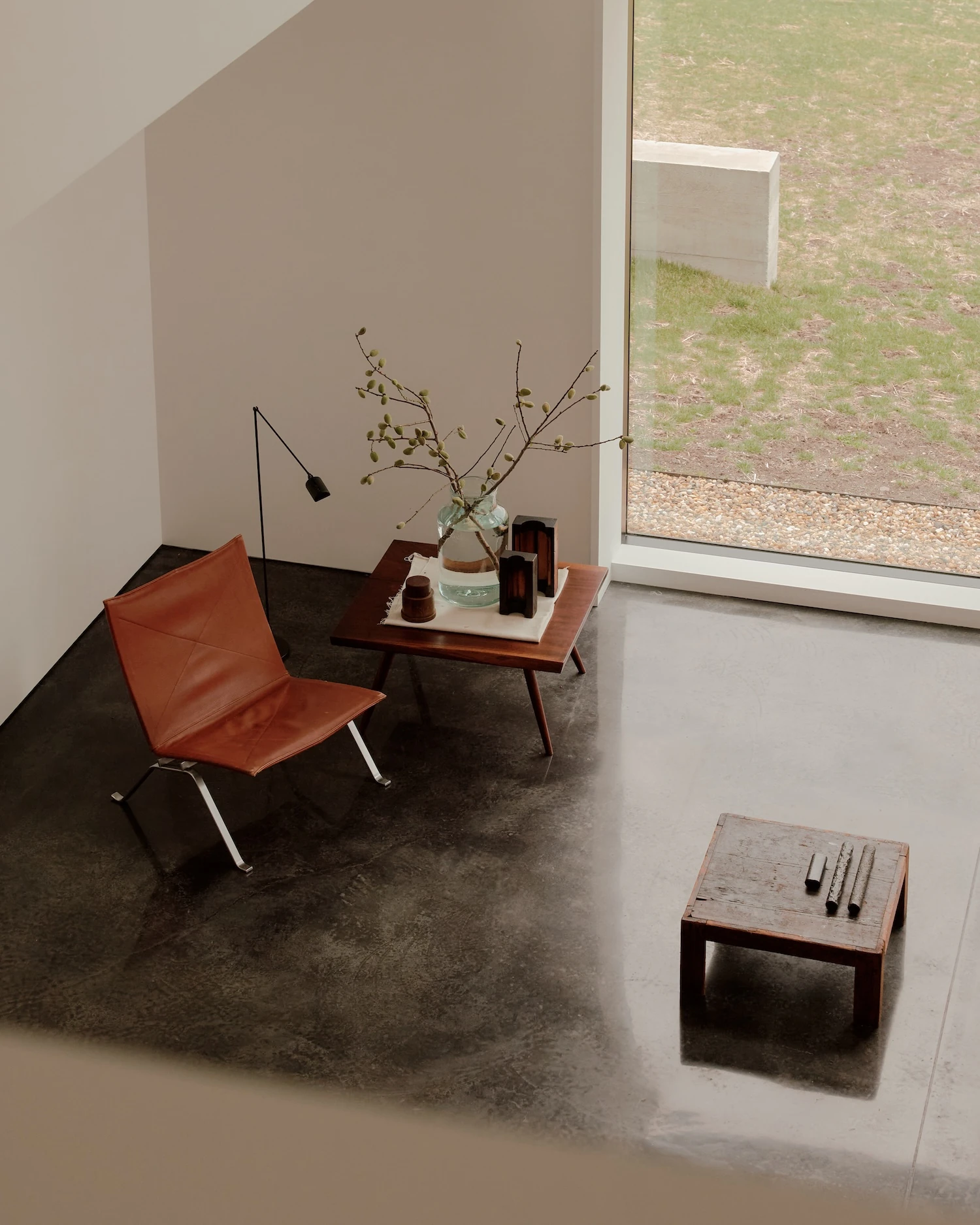 Schoolhouse by JG Neukomm Architecture, photographed by William Jess Laird — Looking down into a corner, a red leather Kjaerholm chair and walnut tables stand on dark stained concrete beside a window onto the lawn.