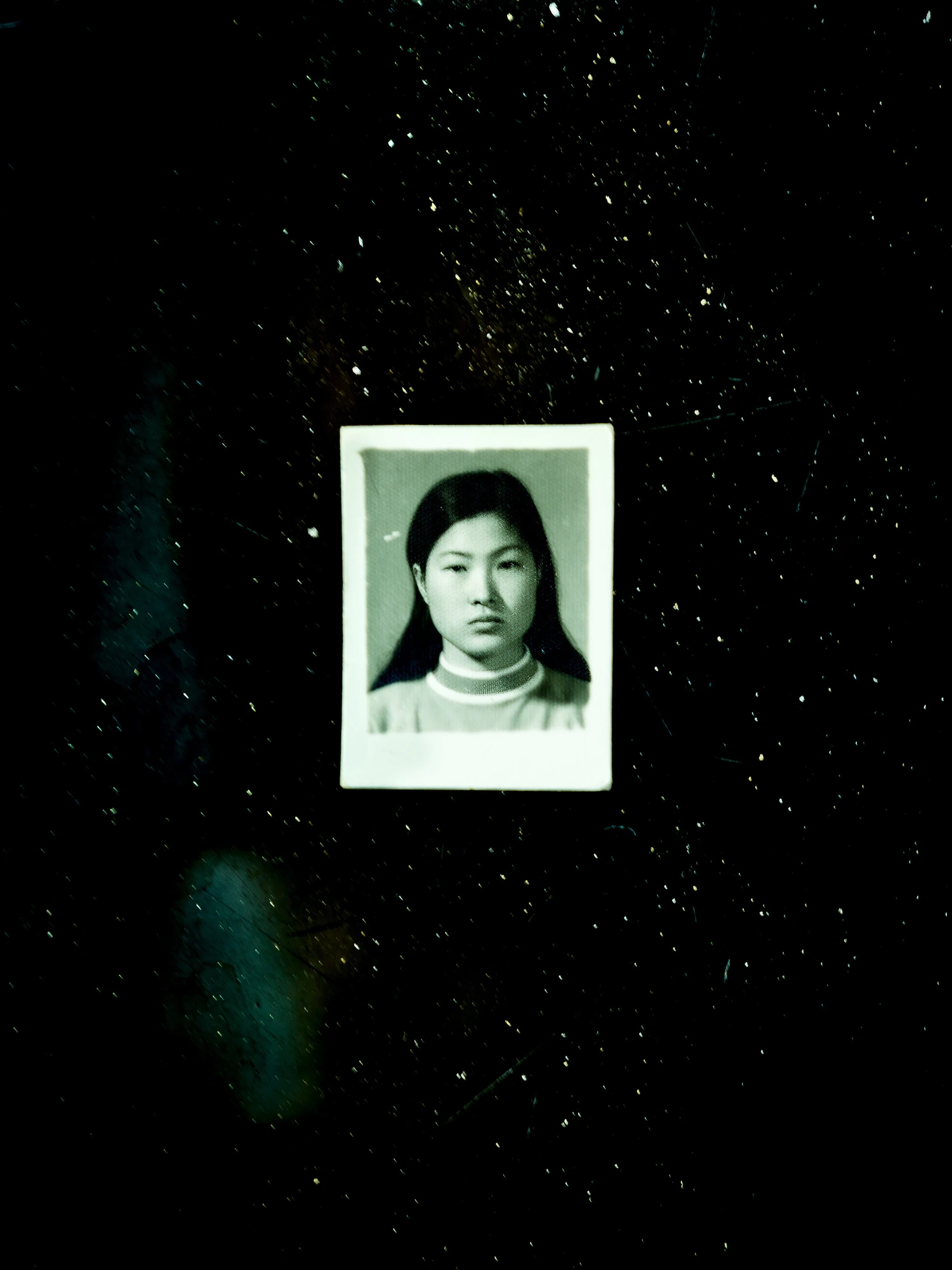 Nirvana by Daesung Lee, photographed by Daesung Lee — A scratched black-and-white identity portrait of a young woman floats in a dark, dust-flecked field.