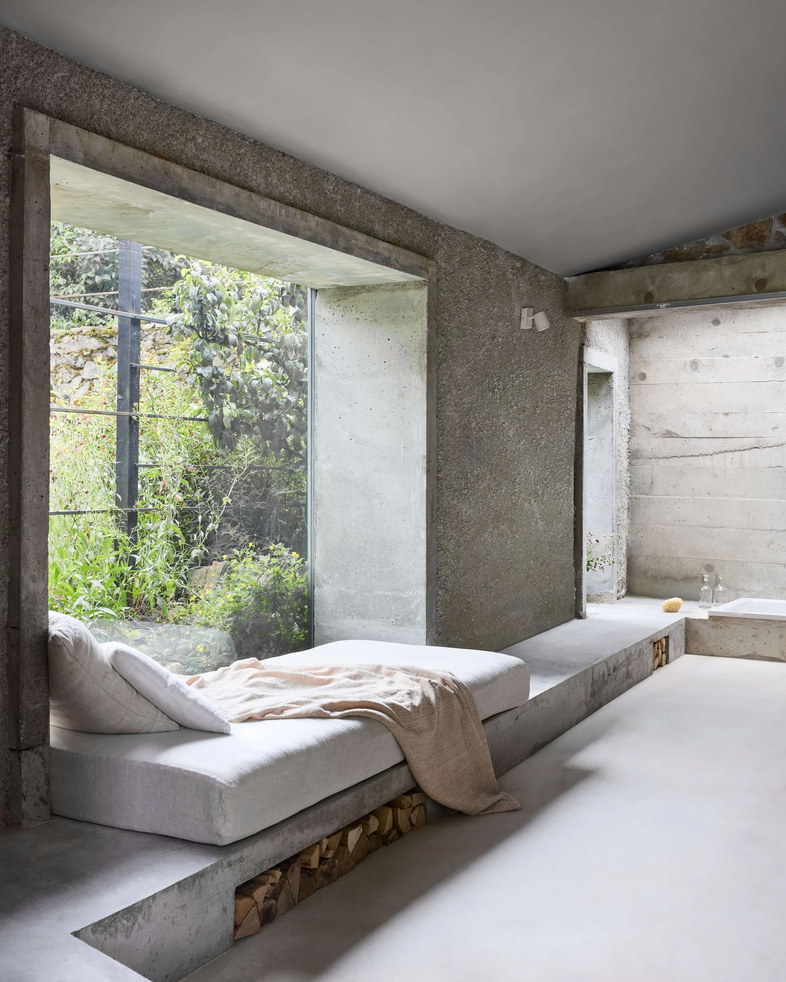 Panoši Újezd Summer House by Lenka Milerová, photographed by Radek Šrettr Úlehla — The long concrete bench steps along the room as daybed and bath surround, split firewood tucked into the open recess below.