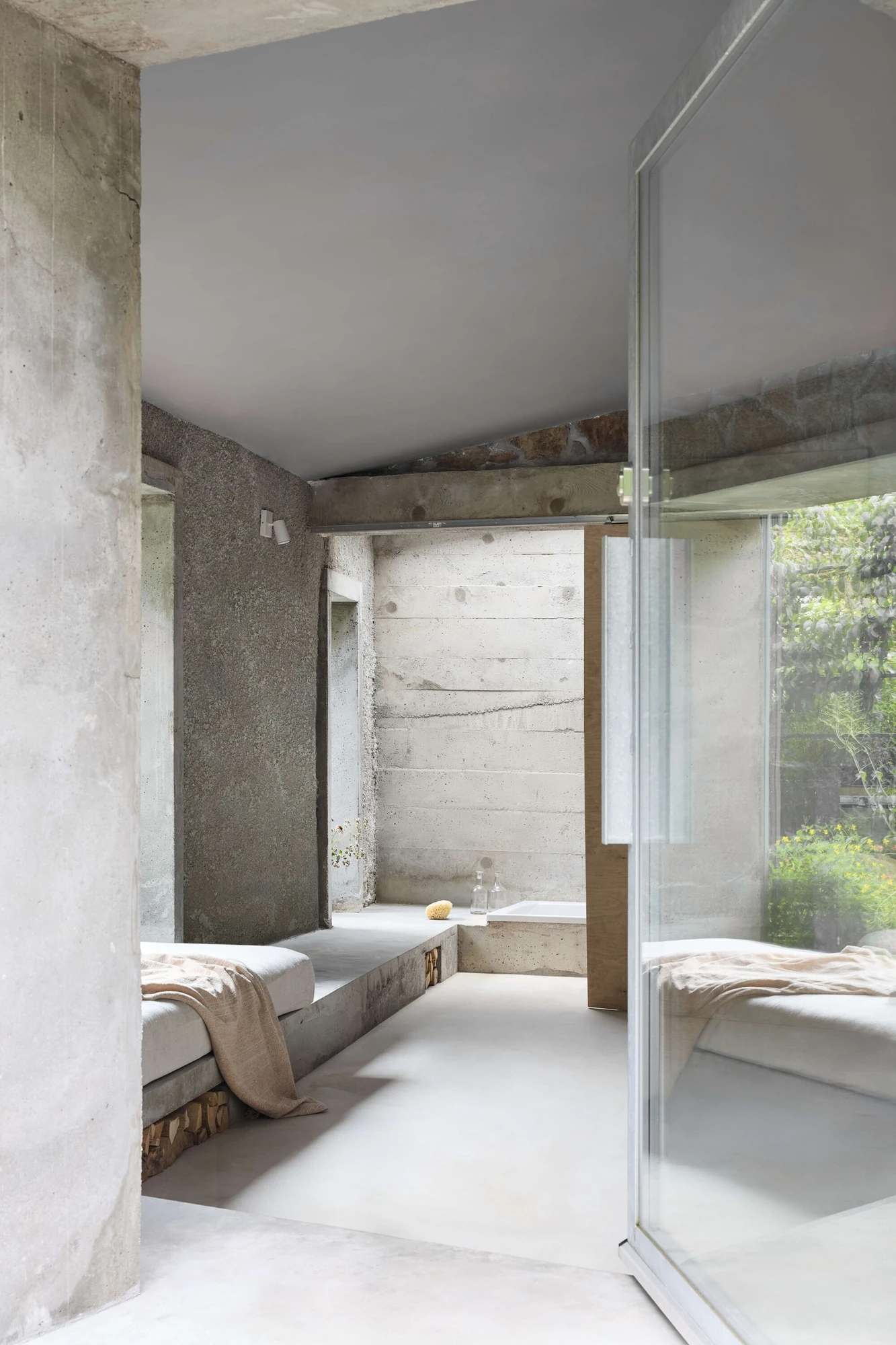 Panoši Újezd Summer House by Lenka Milerová, photographed by Radek Šrettr Úlehla — An interior view across the pale polished concrete floor, board-formed concrete and rough stone walls meeting at a glazed pivot door open to green.