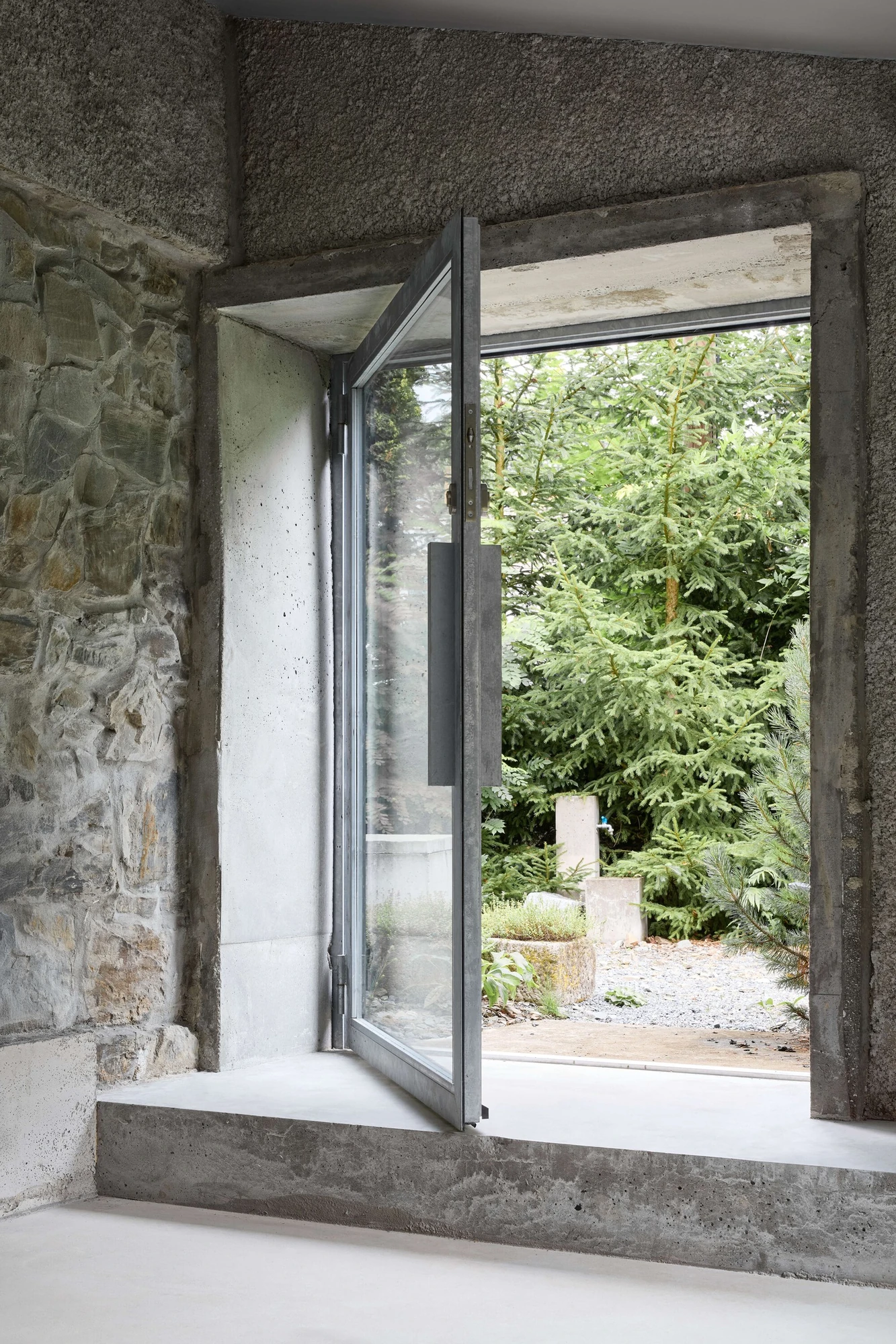 Panoši Újezd Summer House by Lenka Milerová, photographed by Radek Šrettr Úlehla — The same opening with its steel-framed glazed pivot leaf swung open into the garden, stone wall at one side.