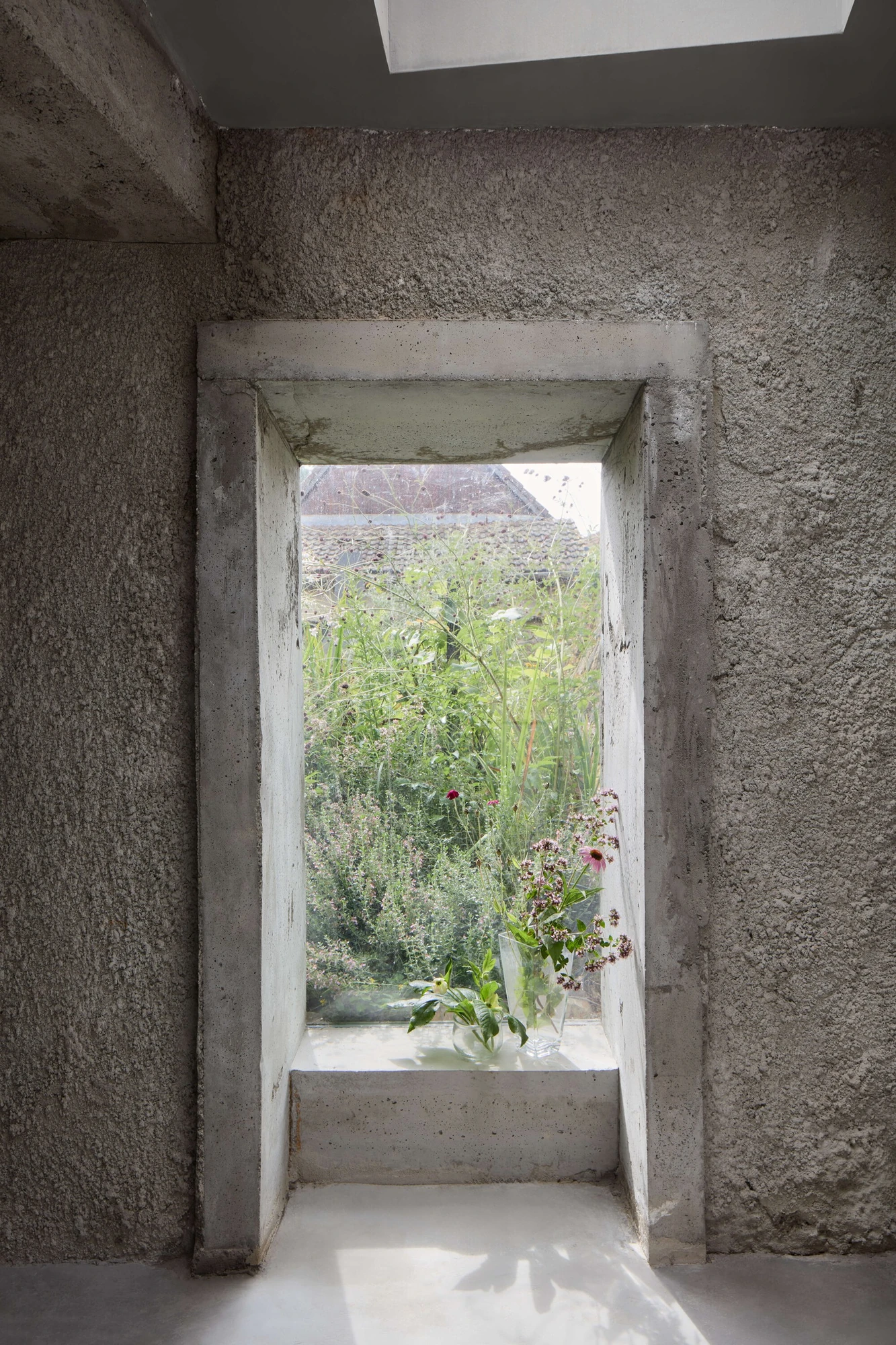 Panoši Újezd Summer House by Lenka Milerová, photographed by Radek Šrettr Úlehla — A narrow full-height concrete-framed opening, lit from a skylight above, frames tall garden plants at its sill.