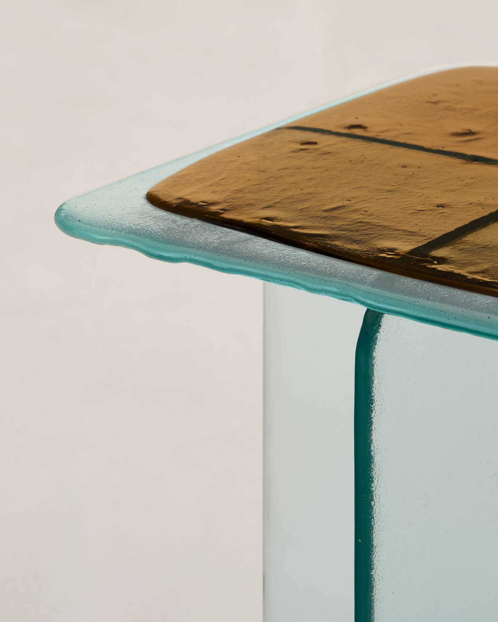 Glacier by Patricia Urquiola — A pair of Glacier side tables photographed frontally, one with a charcoal-grey cast top and one amber, each floating on crossed transparent glass legs against a pale ground.