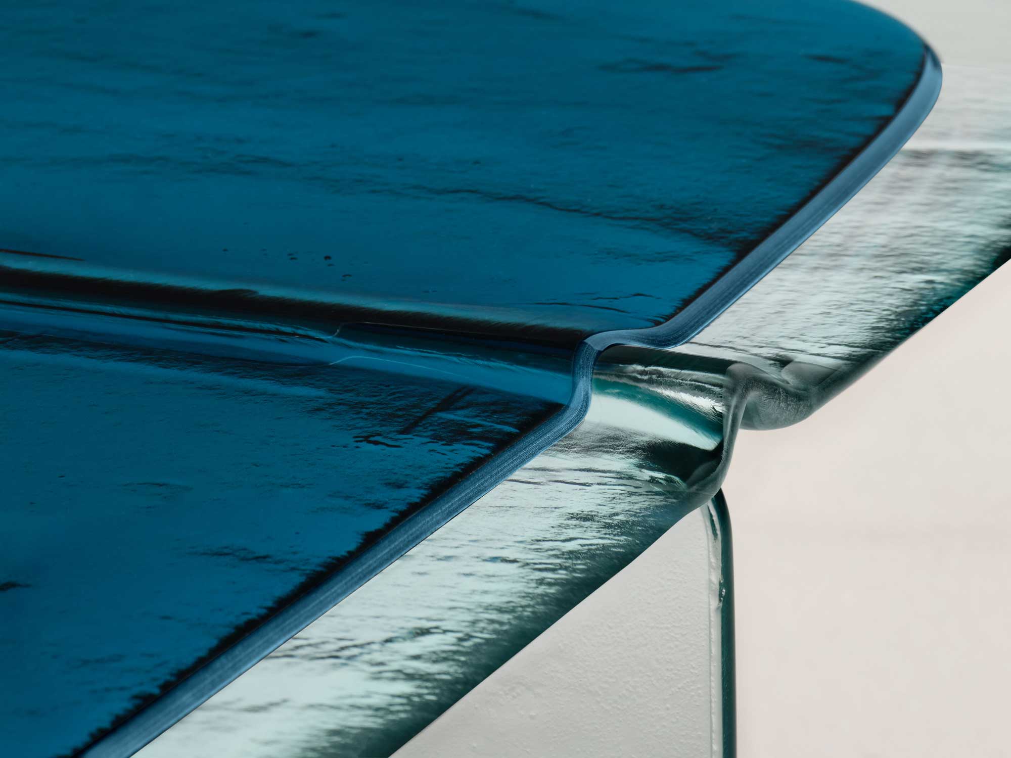 Glacier by Patricia Urquiola — Installation view on a concrete floor: grey and blue Glacier coffee tables with two matching side tables, a dark ceramic vase of dried branches resting on the blue top.