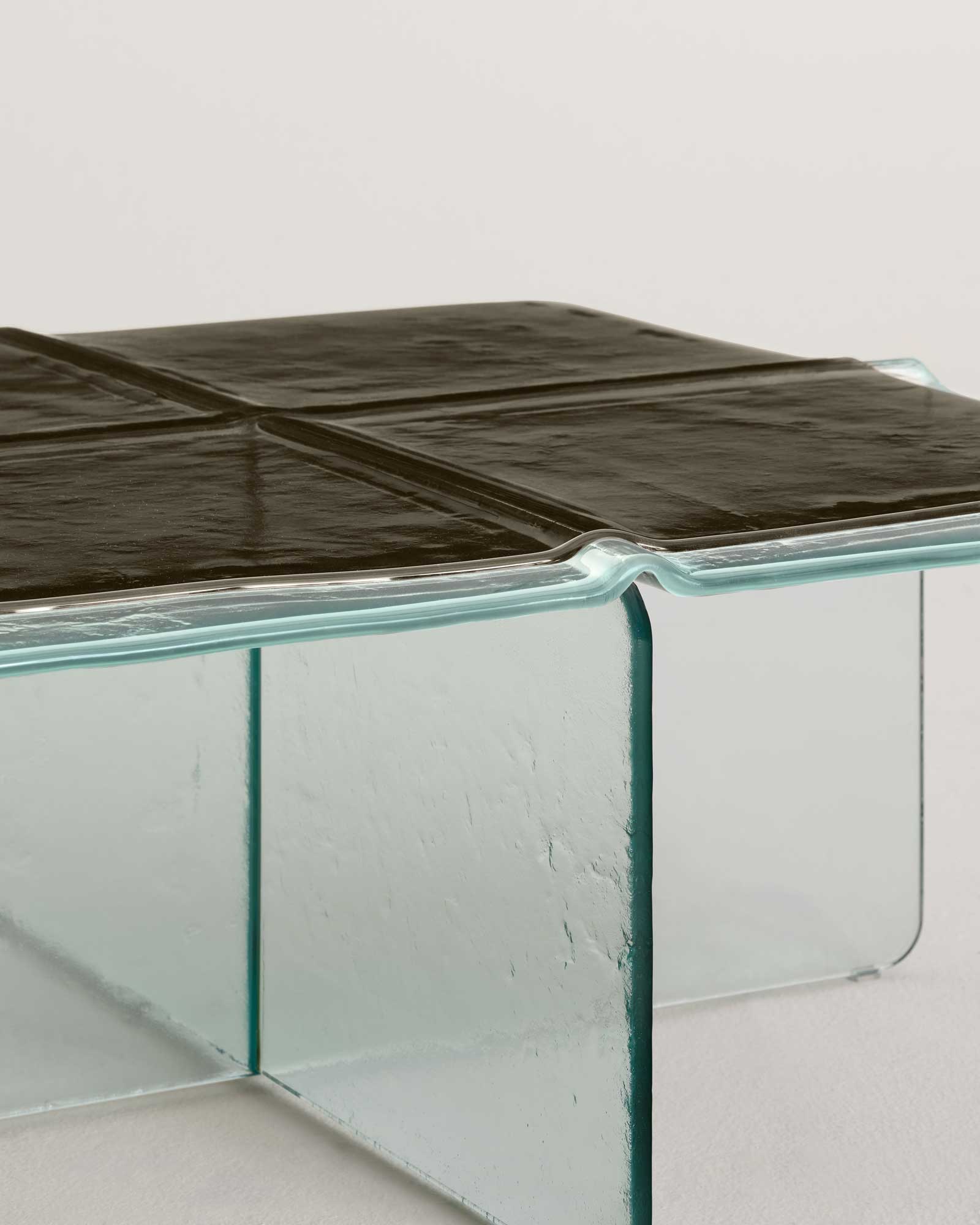 Glacier by Patricia Urquiola — A small square Glacier coffee table with a black four-tile cast top on a transparent X-shaped glass base, isolated on a white seamless ground.