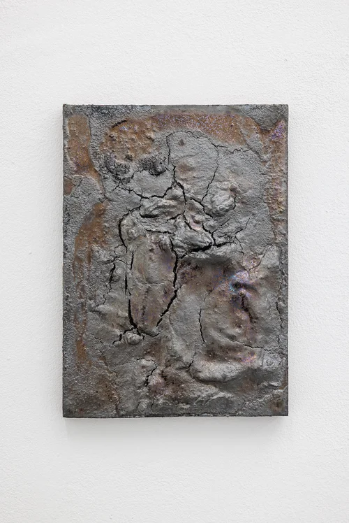 NADIR by Zishi Han and Laurence Sturla — A cracked, metallic relief panel patinated in graphite and rust hangs alone on a white wall, its surface fissured like dried ground.