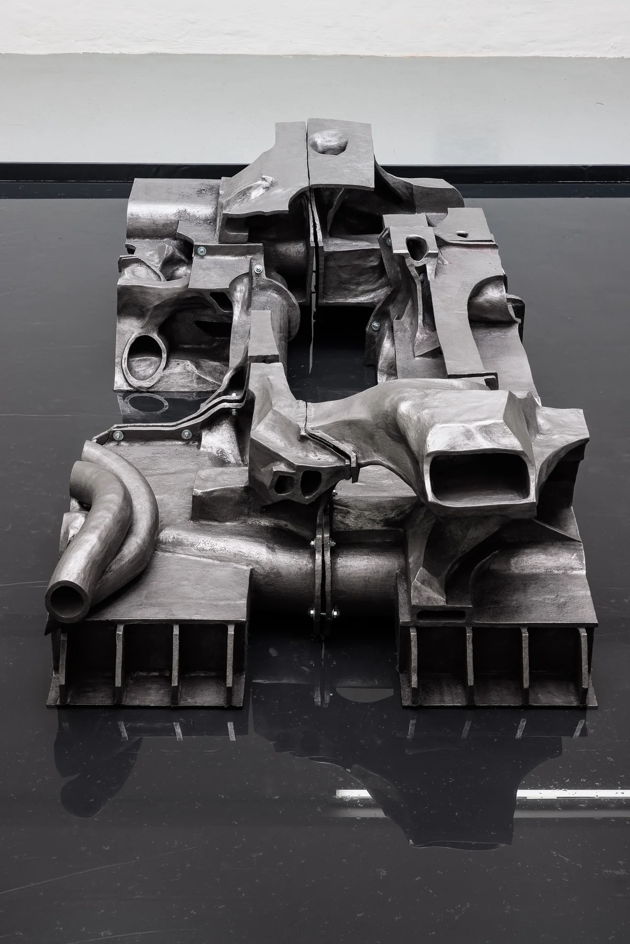 NADIR by Zishi Han and Laurence Sturla — The graphite ceramic seen head-on, part engine, part building, part landscape, reflected in the black pool beneath it.