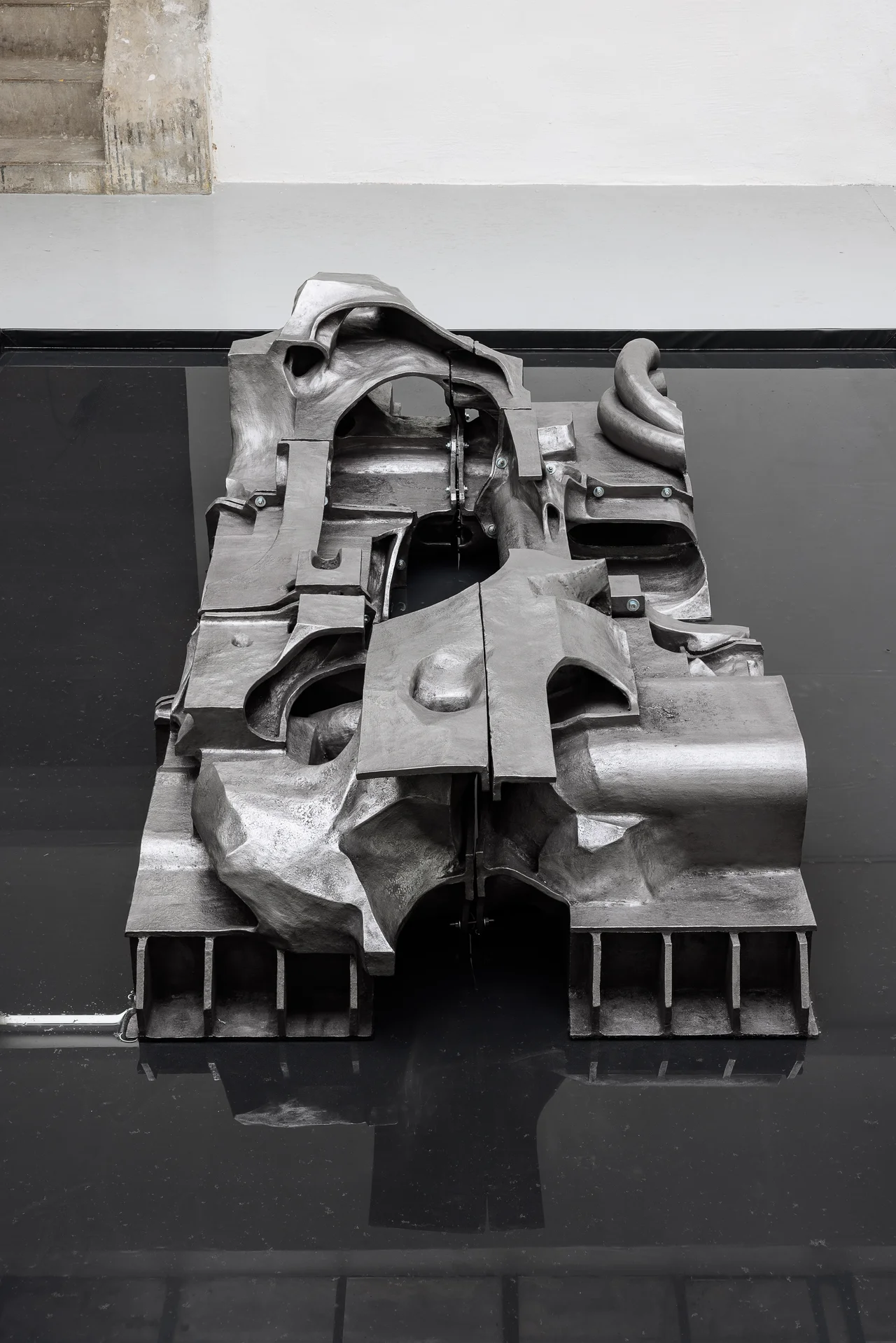 NADIR by Zishi Han and Laurence Sturla — Close view of the graphite-powdered ceramic, its vents, ducts and ribbed underside cast like a wrecked machine on a black mirrored surface.