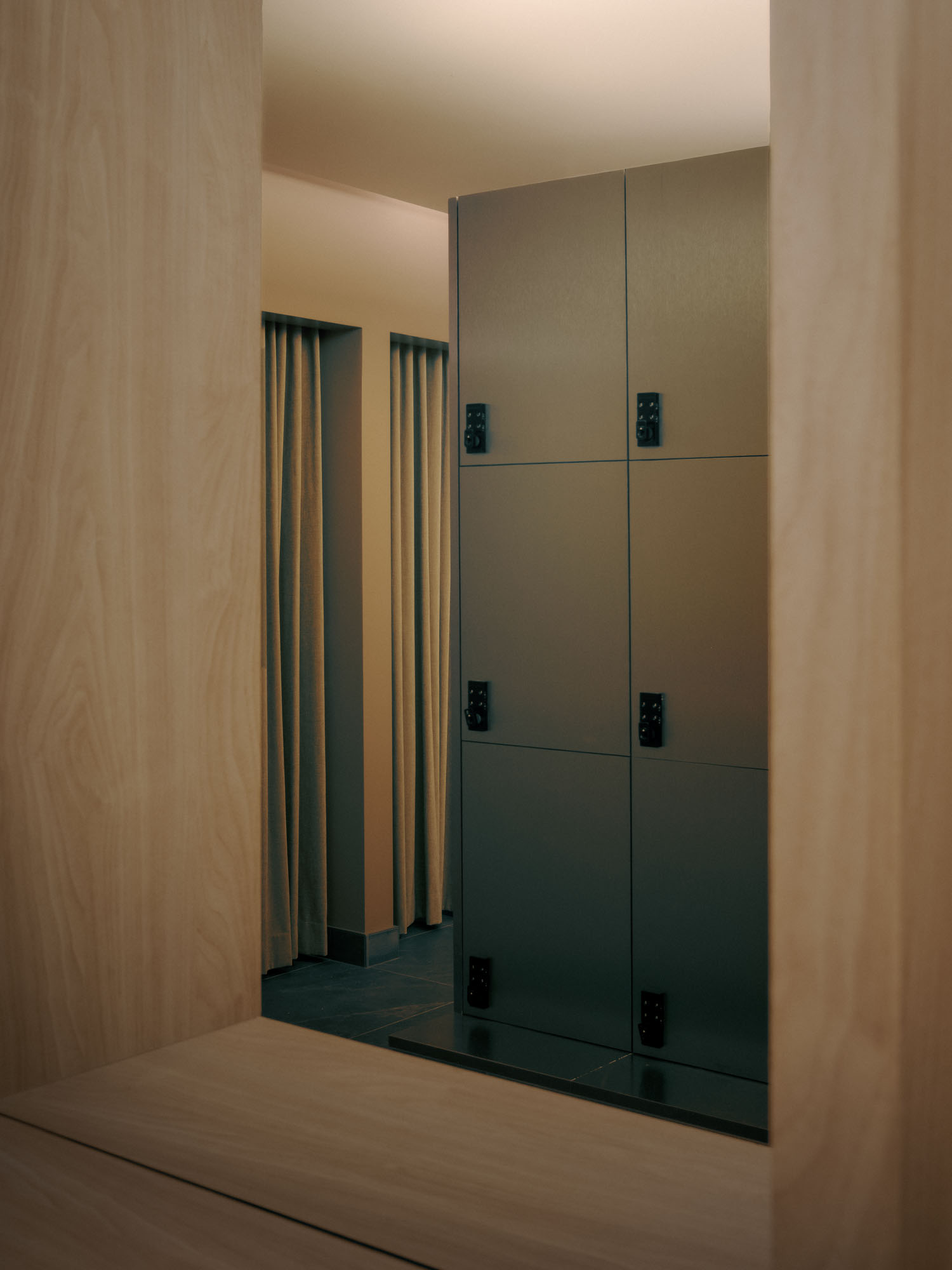 Recess by Future Simple Studio, photographed by Félix Michaud, Recess — Olive-grey metal locker doors face pale oak partitions and linen curtains over a slate floor in the all-gender changing room.