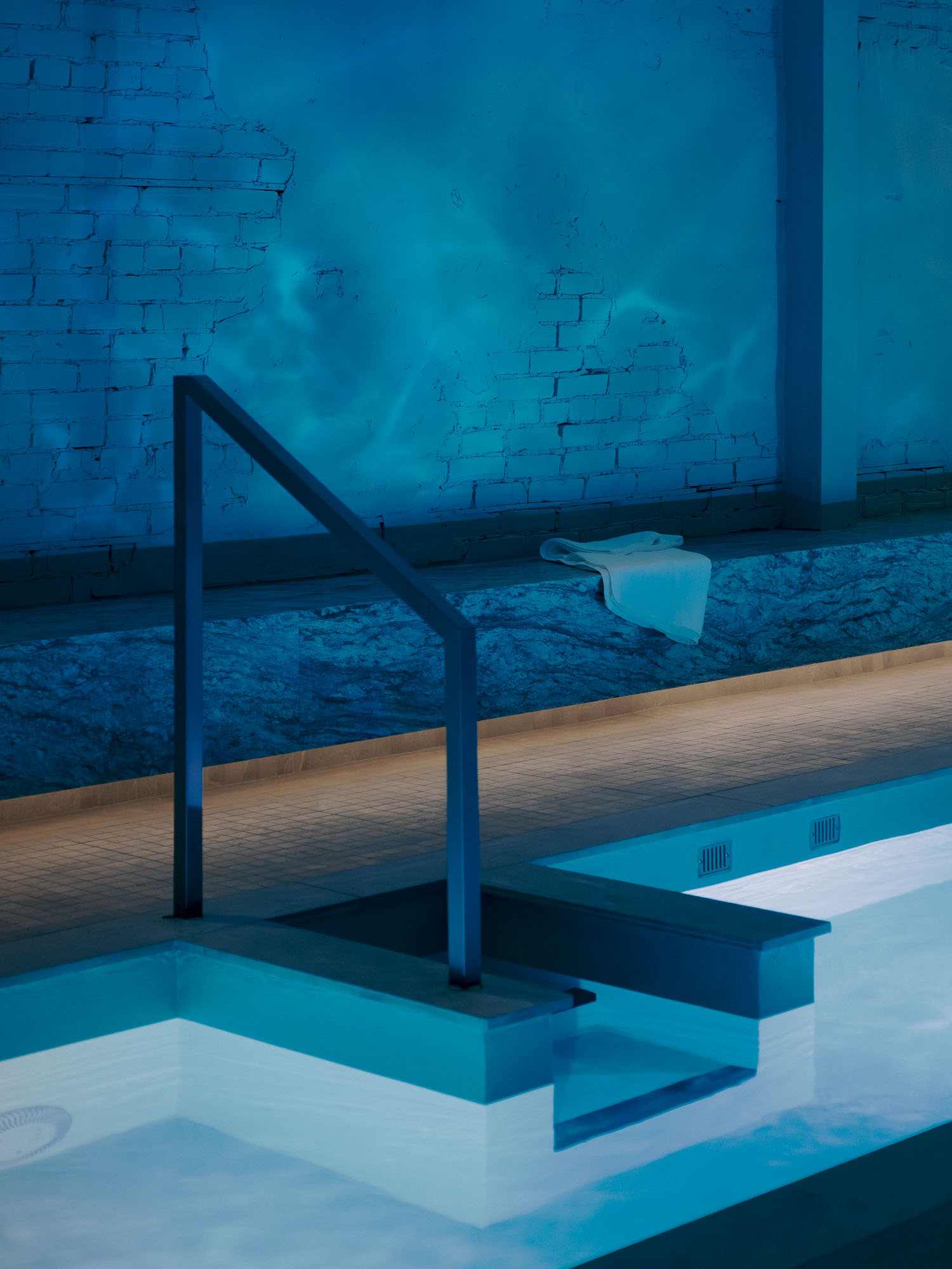 Recess by Future Simple Studio, photographed by Félix Michaud, Recess — A bench of rough-faced marble runs beneath plaster walls lit by paired Bocci sconces, slender columns rising past a curved timber wall in the relaxation area.