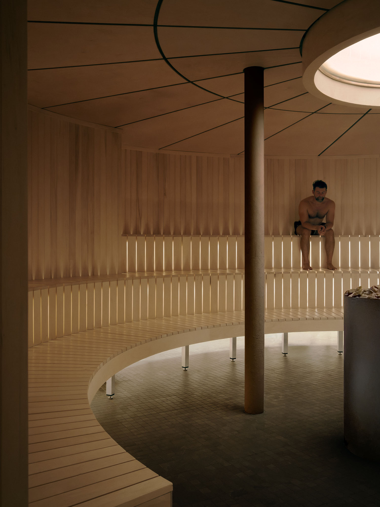 Recess by Future Simple Studio, photographed by Félix Michaud, Recess — A curved plywood wall throws a warm cove-lit line along a grey mosaic floor, a slice of the cold zone's blue visible in the gap beyond.