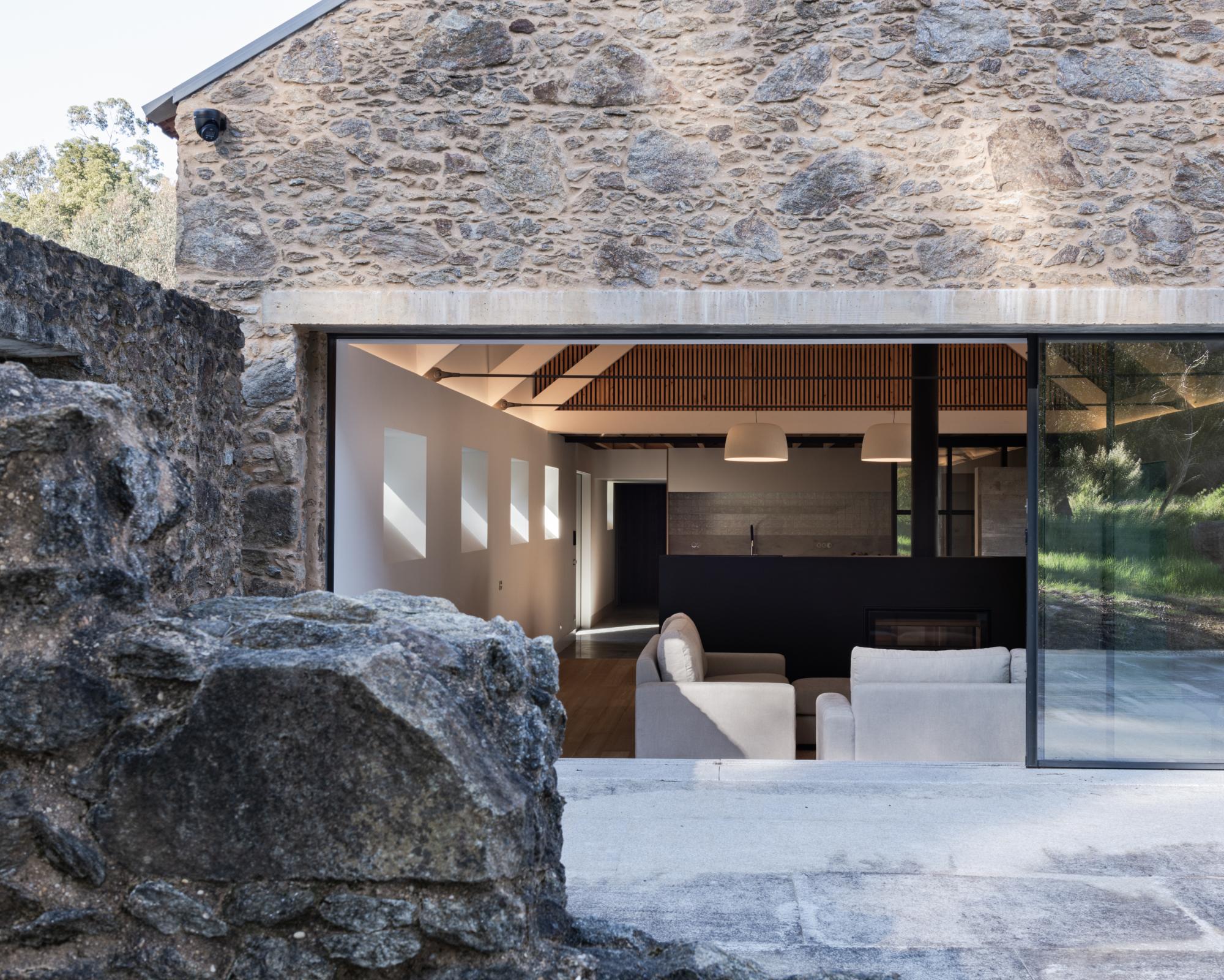 Single-Family Home by Branco del Rio Arquitectos, photographed by Frederico Martinho — In a circulation space, Douglas fir joists run beneath a raw stone soffit, white plaster meeting exposed granite above a timber floor and a granite step, a bedroom…
