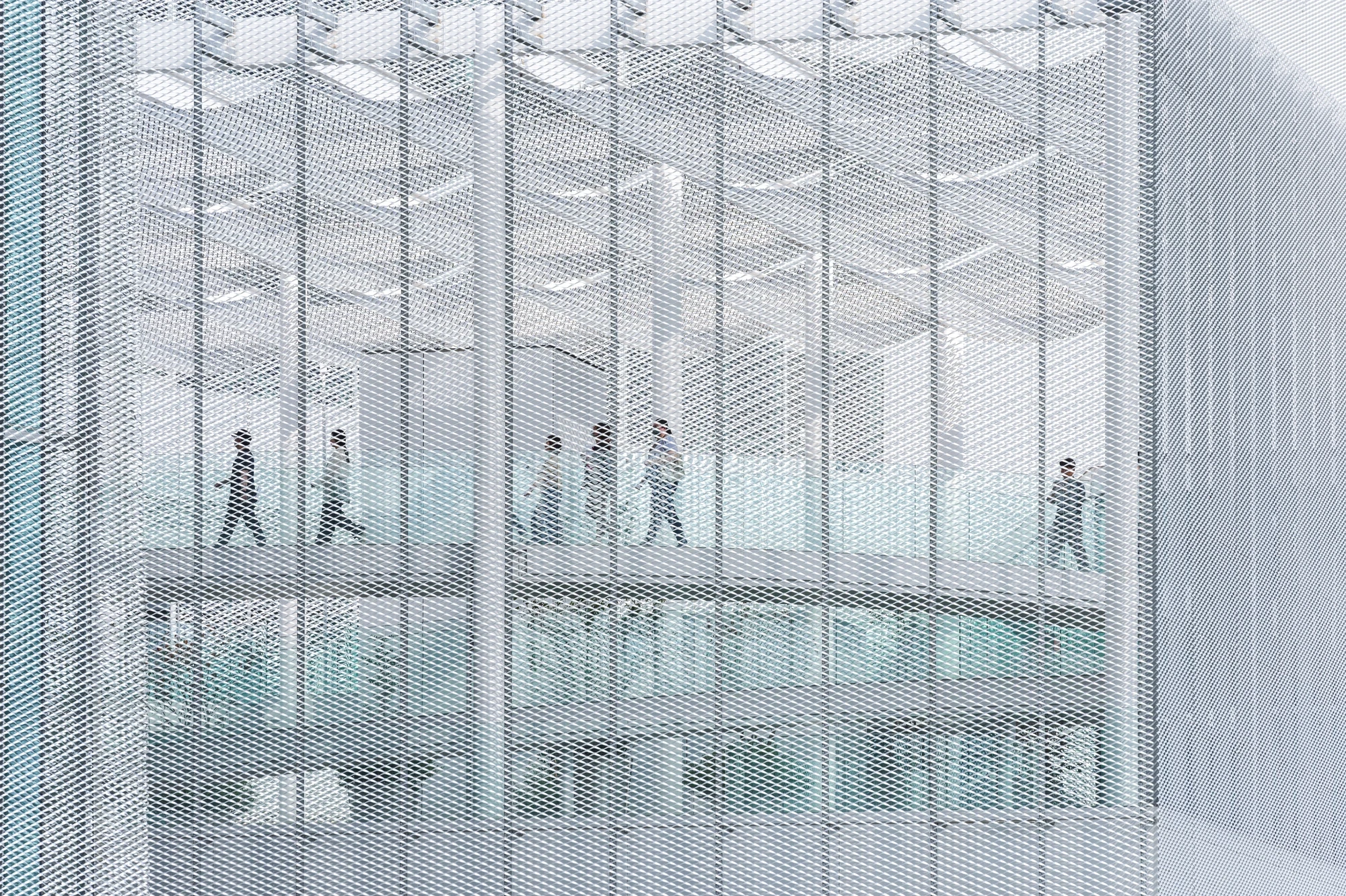Taichung Art Museum by SANAA, photographed by Yi-Hsien Lee (YHLAA) — Behind a semi-transparent mesh and glass facade, a line of visitors crosses an interior bridge as silhouettes.