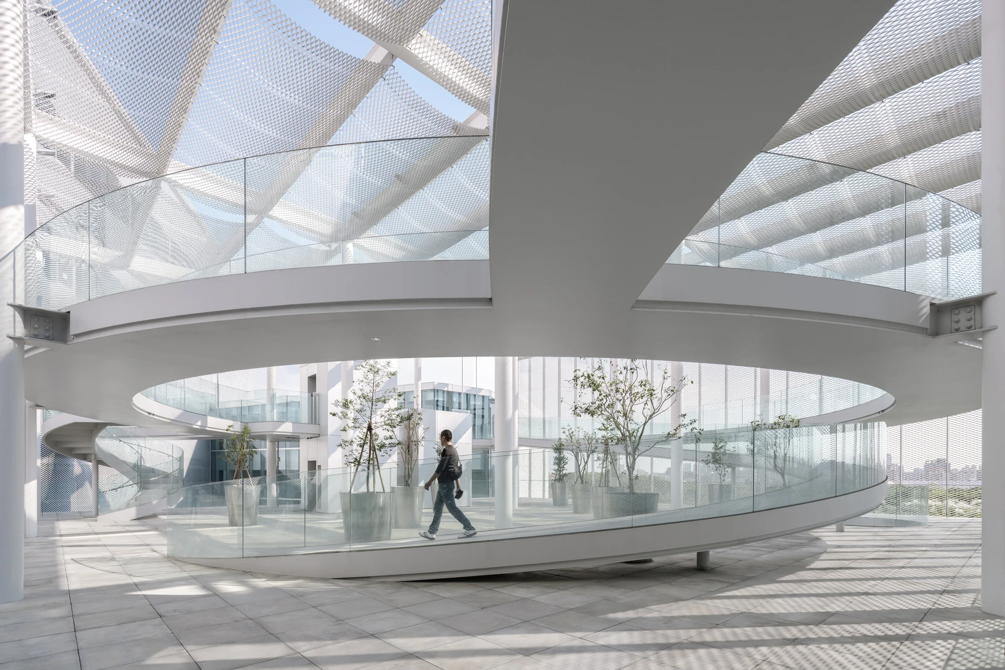 Taichung Art Museum by SANAA, photographed by Yi-Hsien Lee (YHLAA) — On the rooftop cultural forest, spiraling ramps curve beneath a draped expanded-metal-mesh canopy carried on bolted white steel beams, with potted trees over stone pavers.