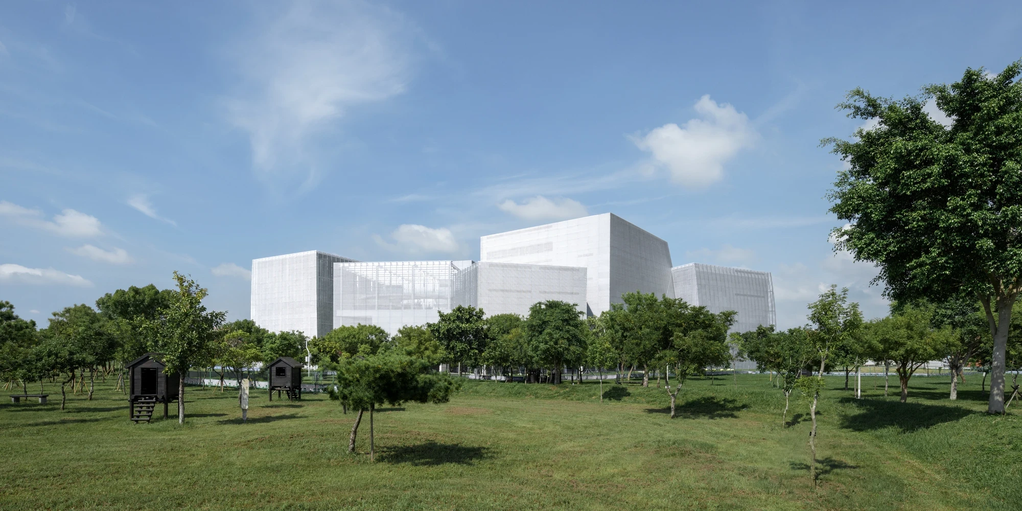 Taichung Art Museum by SANAA, photographed by Yi-Hsien Lee (YHLAA) — Seen across the park, the museum reads as a cluster of faceted silver-mesh volumes under an open sky, ringed by young trees.