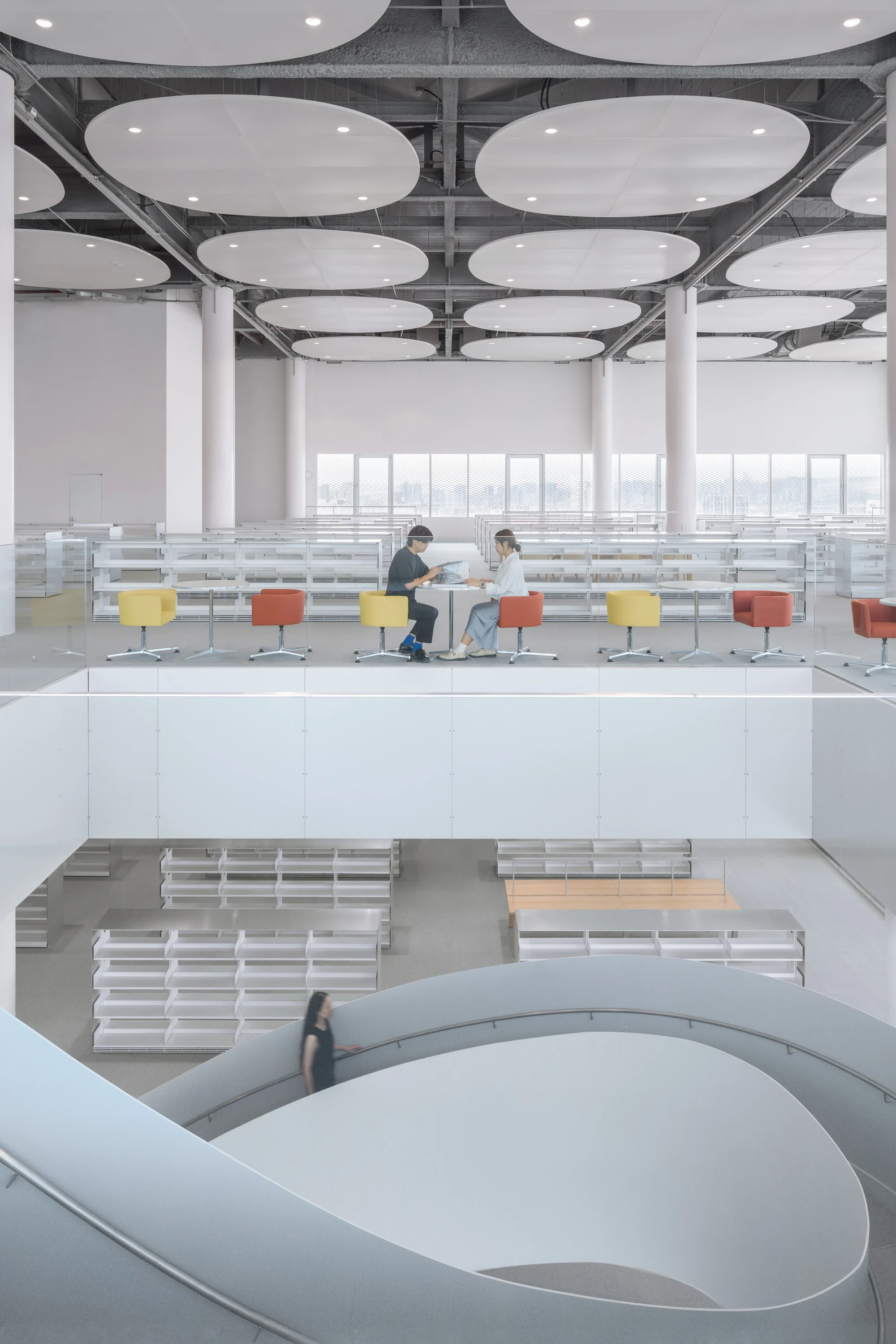 Taichung Art Museum by SANAA, photographed by Yi-Hsien Lee (YHLAA) — Oval acoustic discs float below the exposed services of the library, over colored reading chairs and a void down to the lower level.