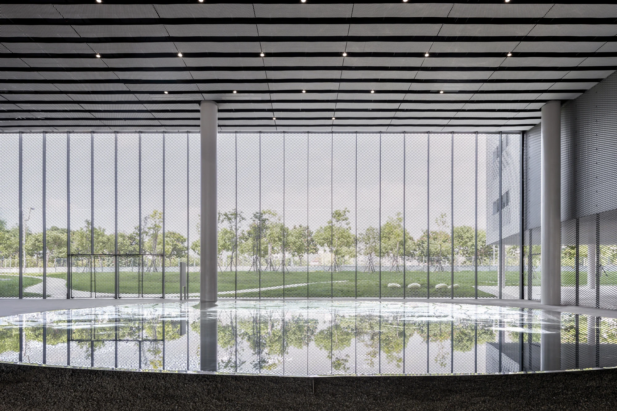Taichung Art Museum by SANAA, photographed by Yi-Hsien Lee (YHLAA) — A ground-level room meets a full-height glass wall and a reflecting pool, its black slatted ceiling mirrored in the still water.